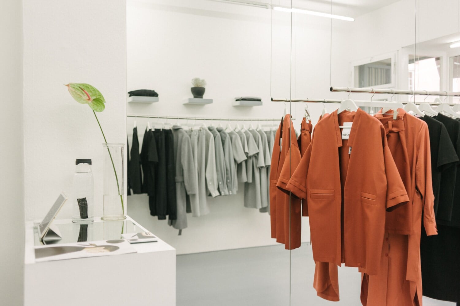 Puristische, elegante Kleidungsstücke, nach Farben sortiert, auf hängenden Kleiderstangen in einer Boutique. Puristische, elegante Kleidungsstücke, nach Farben sortiert, auf hängenden Kleiderstangen in einer Boutique.