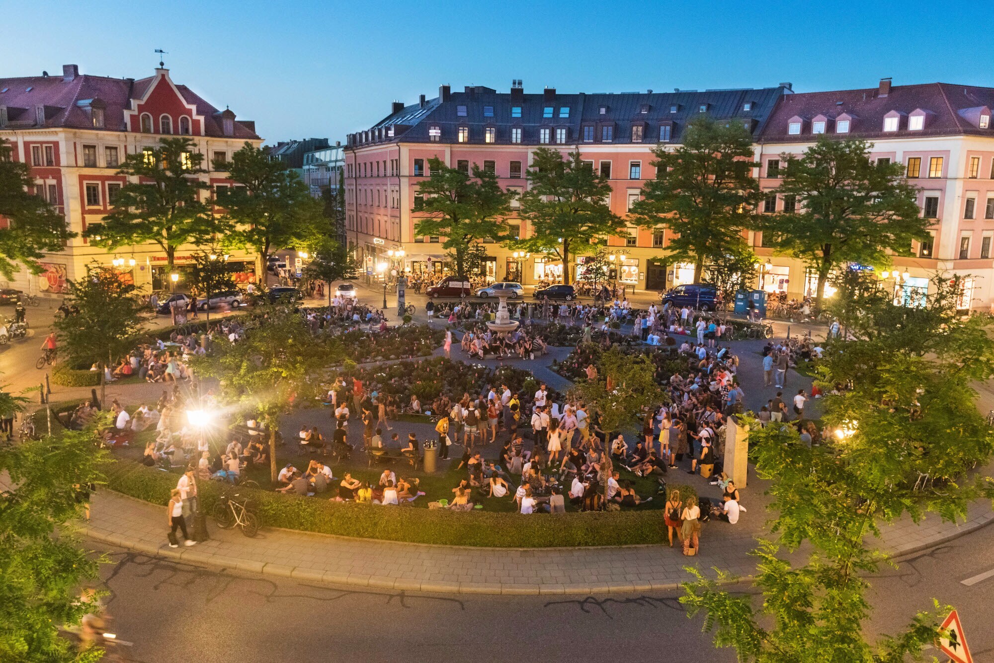 Ein belebter, runder Stadtteilplatz, umgeben von Altbauten am Abend. Ein belebter, runder Stadtteilplatz, umgeben von Altbauten am Abend.