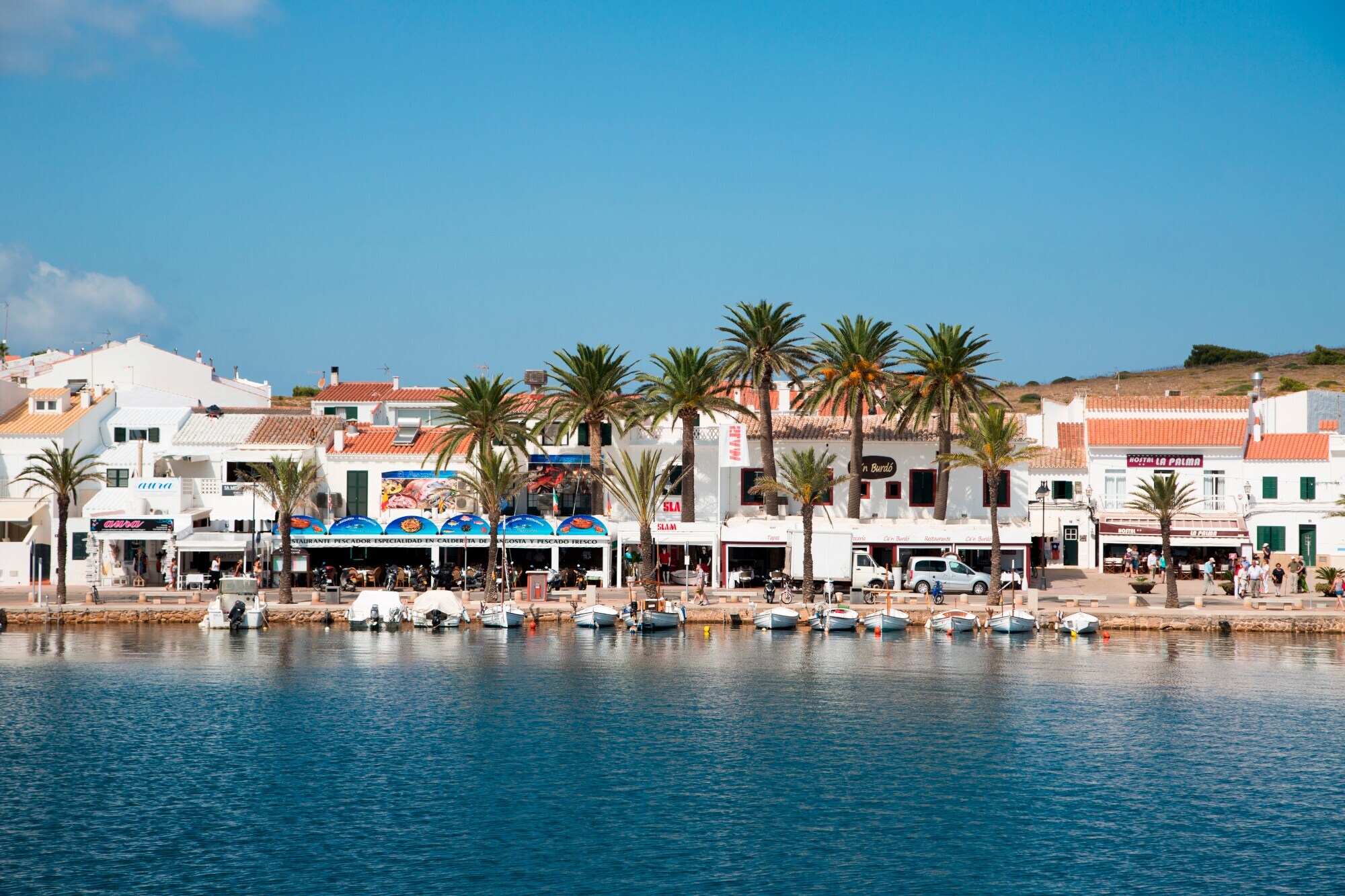Eine Wasserpromenade, an der einige Boote angelegt haben, mit Häusern und Palmen im Hintergrund. Eine Wasserpromenade, an der einige Boote angelegt haben, mit Häusern und Palmen im Hintergrund.
