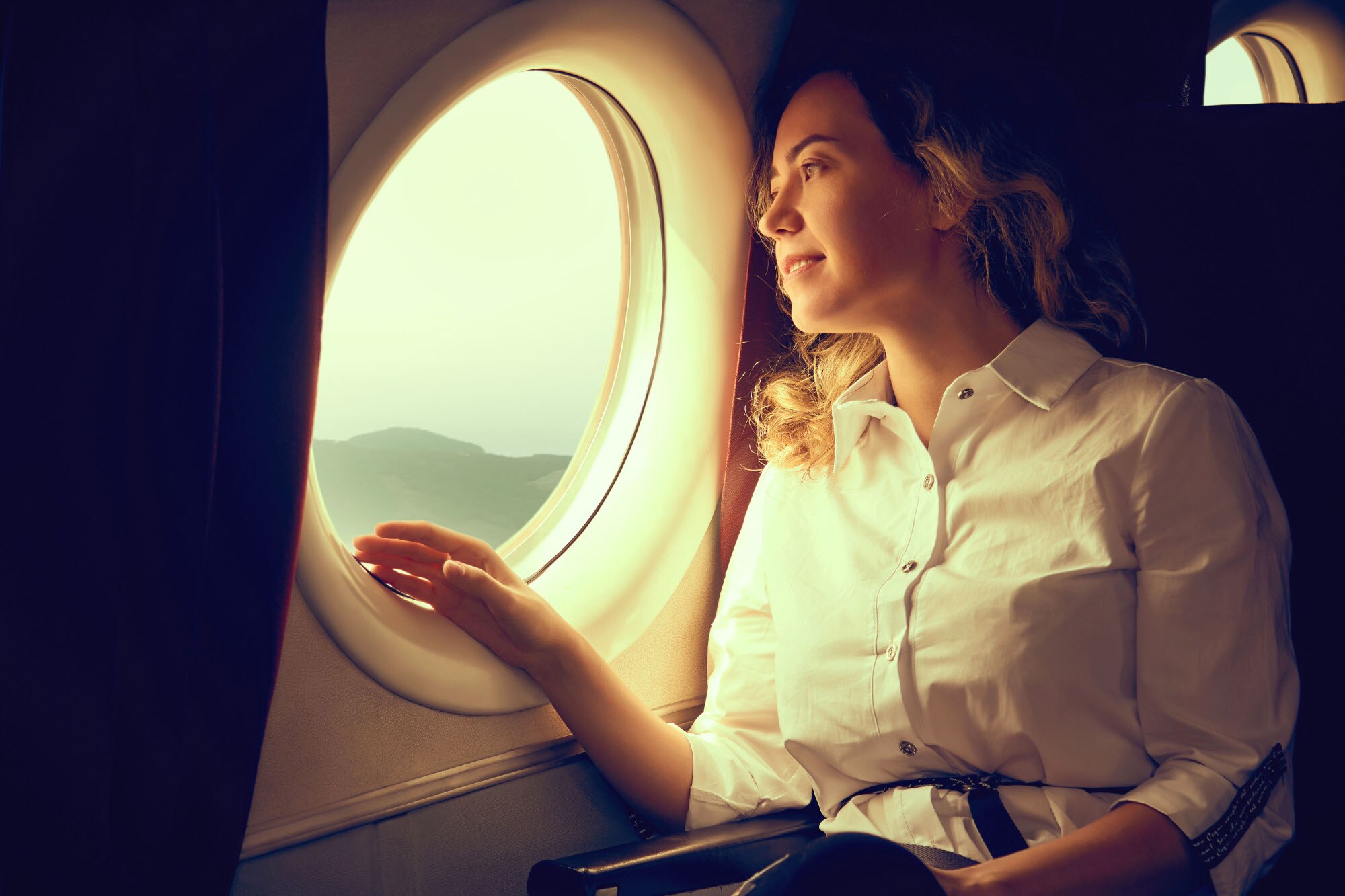 Eine junge Frau in weißer Bluse schaut aus dem Fenster eines Flugzeuges auf eine Landschaft. Eine junge Frau in weißer Bluse schaut aus dem Fenster eines Flugzeuges auf eine Landschaft.