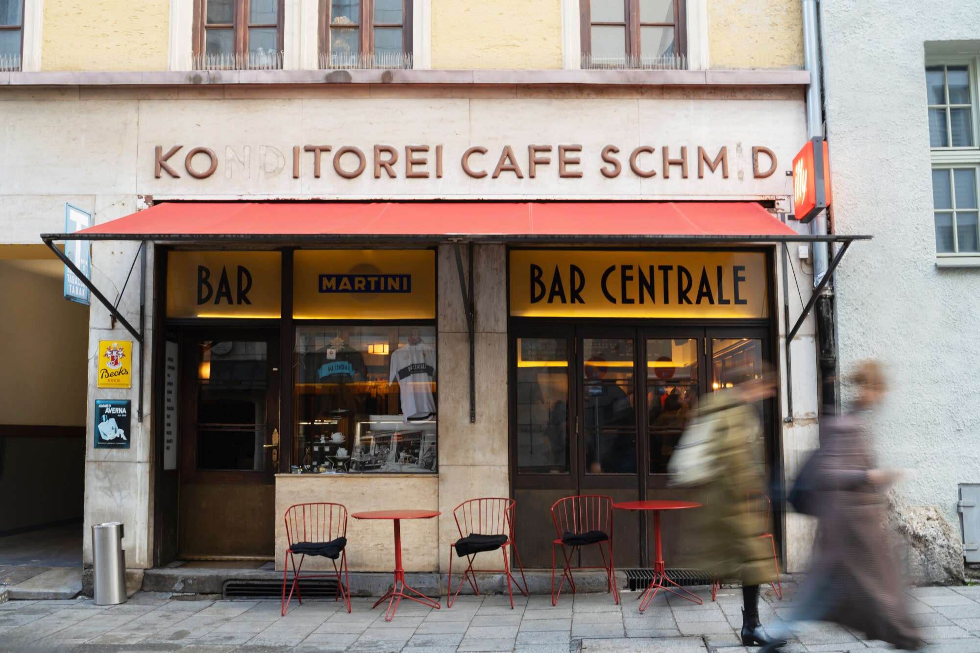 Außenansicht der Bar Centrale mit roter Markise sowie Bistrotischen und Stühlen.