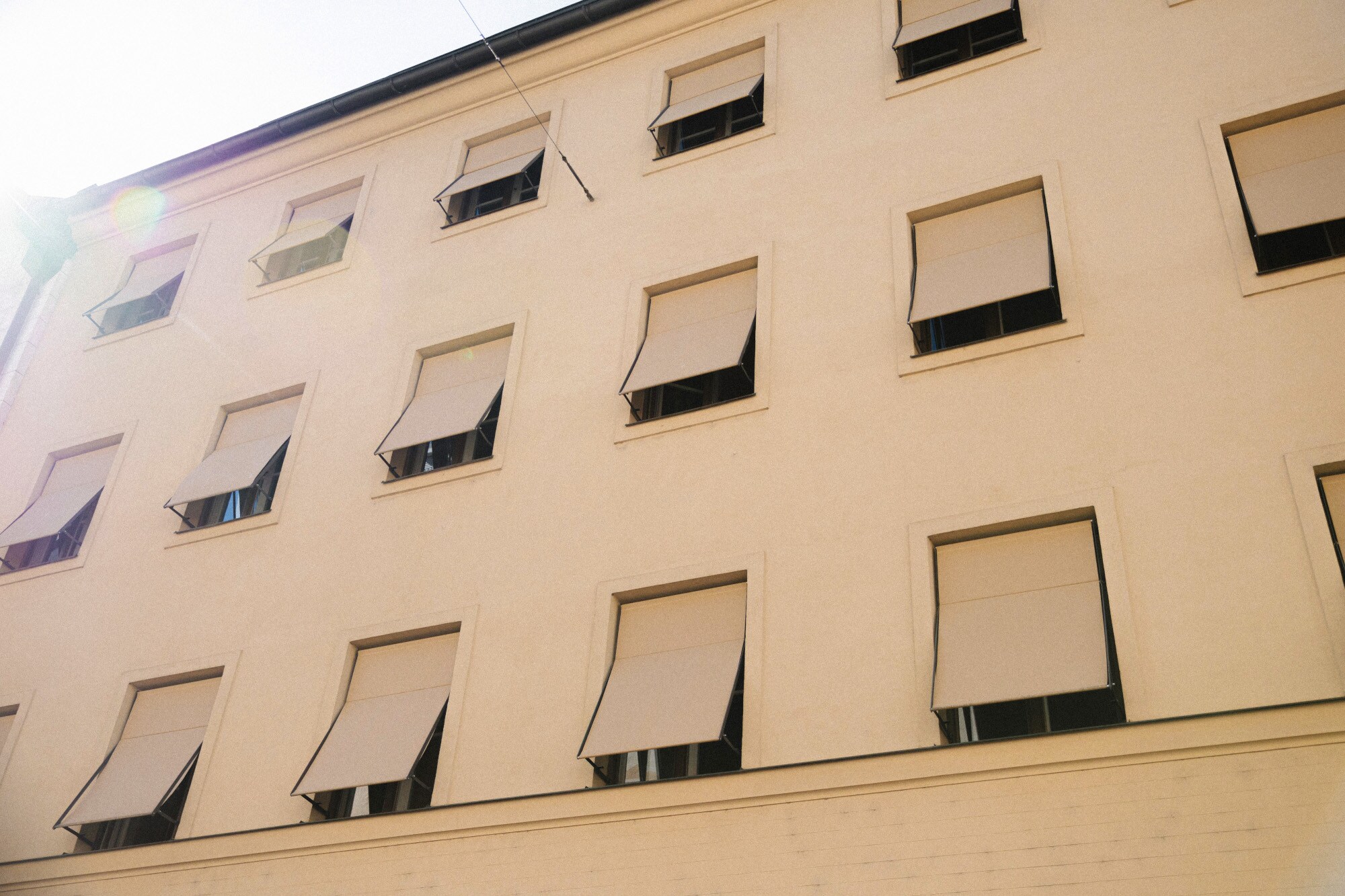 Hellbeige Hausfassade mit gleichfarbigen Markisen vor den Fenstern.