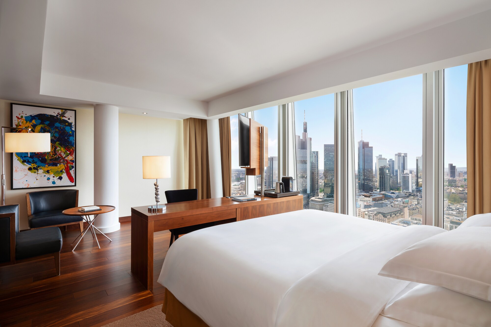 Modernes Hotelzimmer mit Blick auf die Frankfurter Skyline durch bodentiefe Panoramafenster.