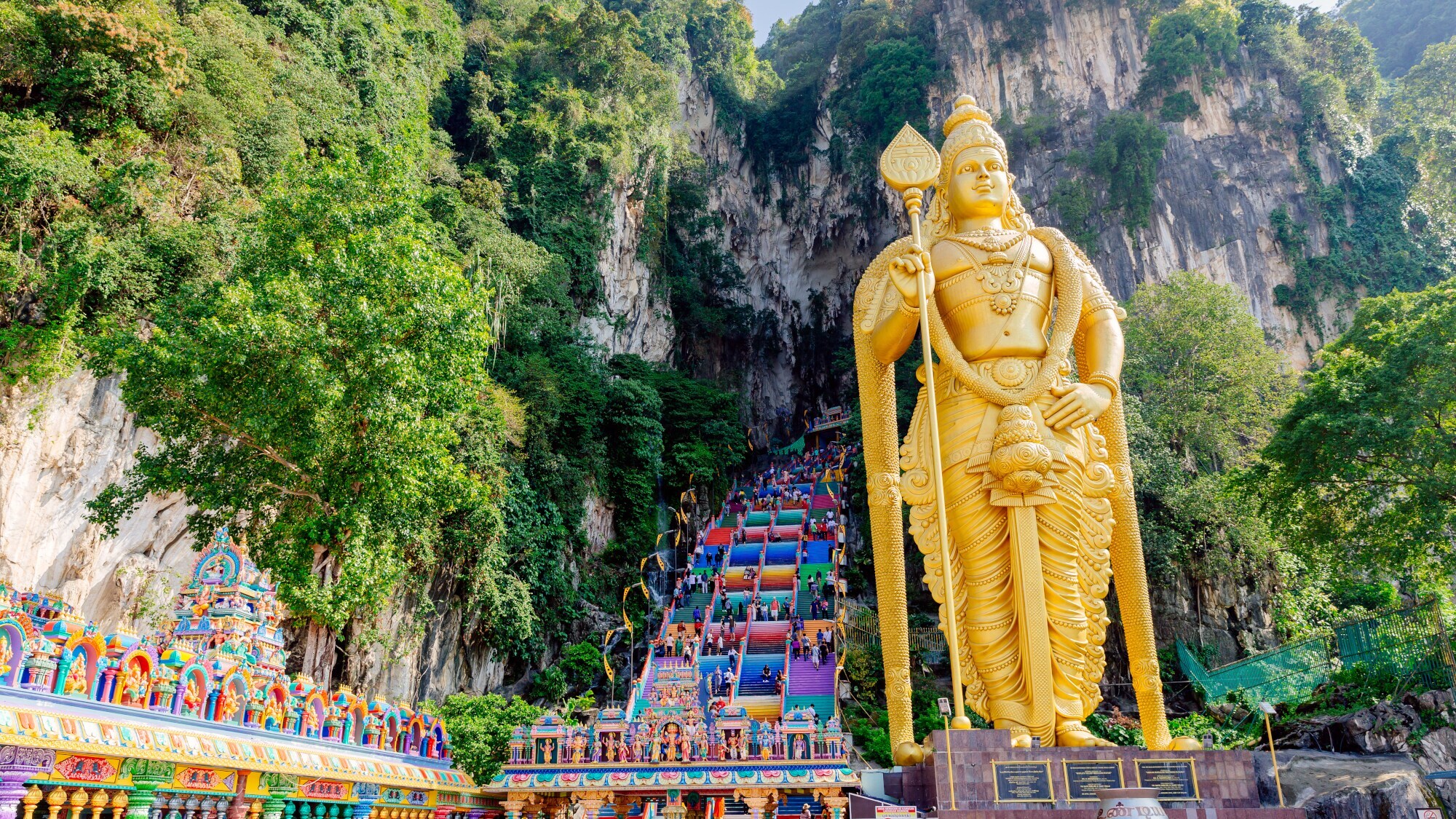 Goldene Statue vor einer großen Treppe mit bunten Stufen, die in eine Felsenhöhle hineinführen.