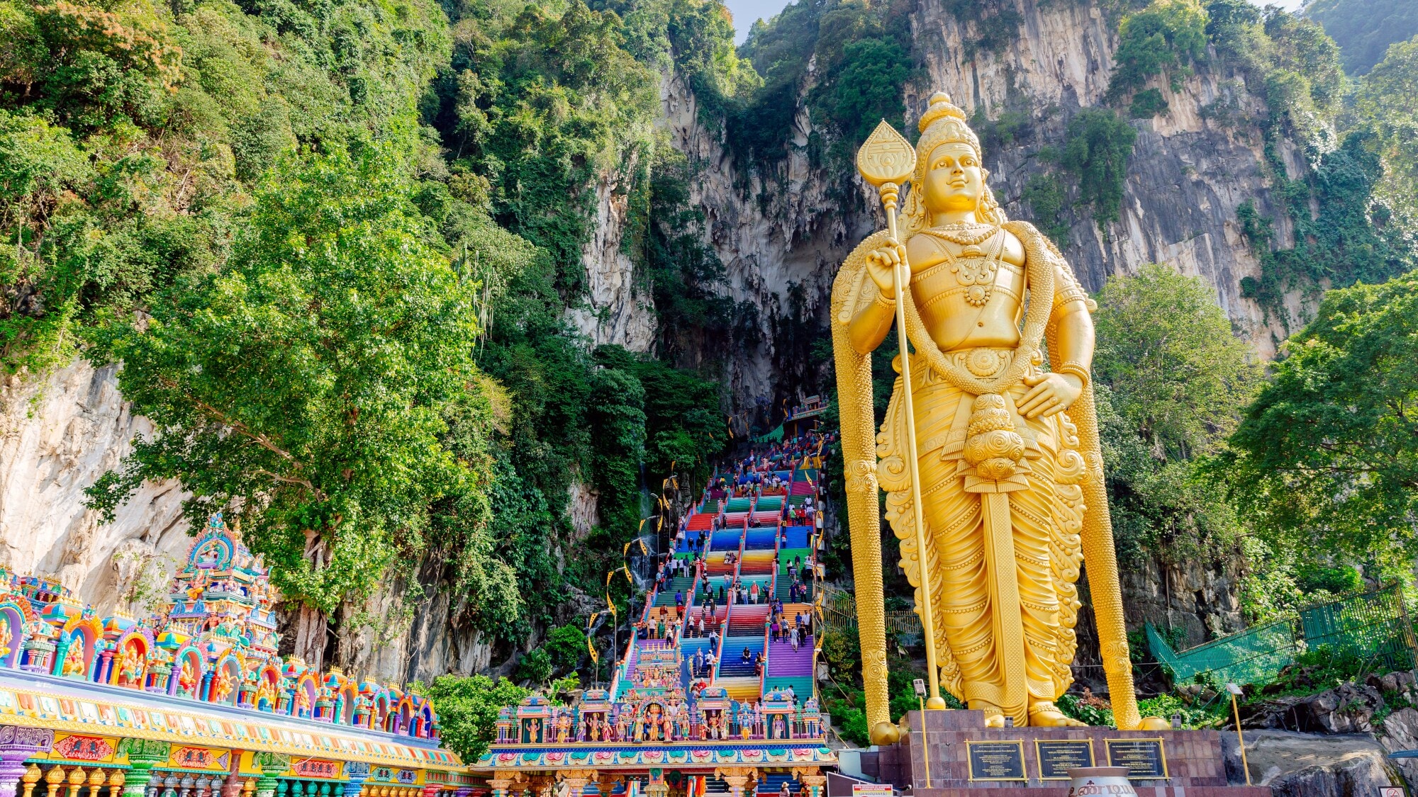 Goldene Statue vor einer großen Treppe mit bunten Stufen, die in eine Felsenhöhle hineinführen. Goldene Statue vor einer großen Treppe mit bunten Stufen, die in eine Felsenhöhle hineinführen.