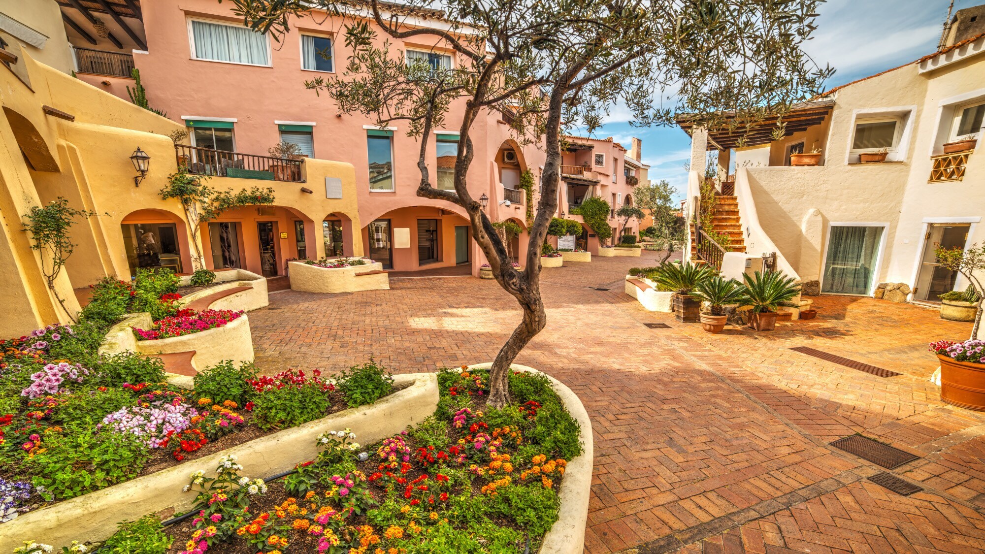 Ein sehr gepflegter Marktplatz auf Sardinien mit pastellfarbenen Häuserfassaden und Blumenbeeten