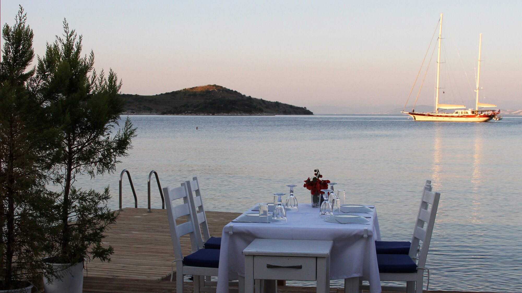 ein fein gedeckter Tisch auf einem Steg am Meer mit einem Boot im Hintergrund.
