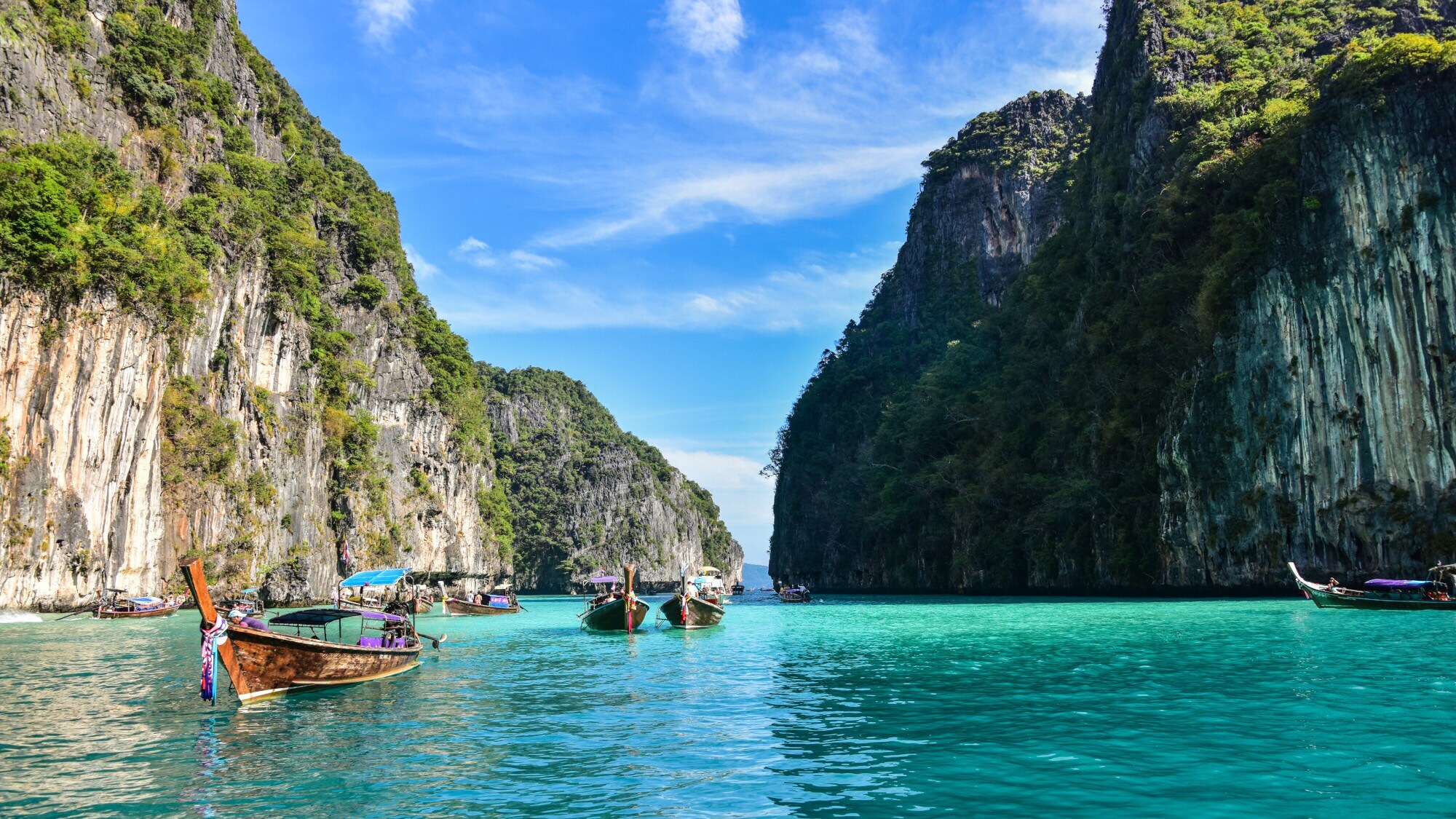 Boote in einer Lagune im türkisblauen Meer mit grün bewachsenen Felsen im Hintergrund.