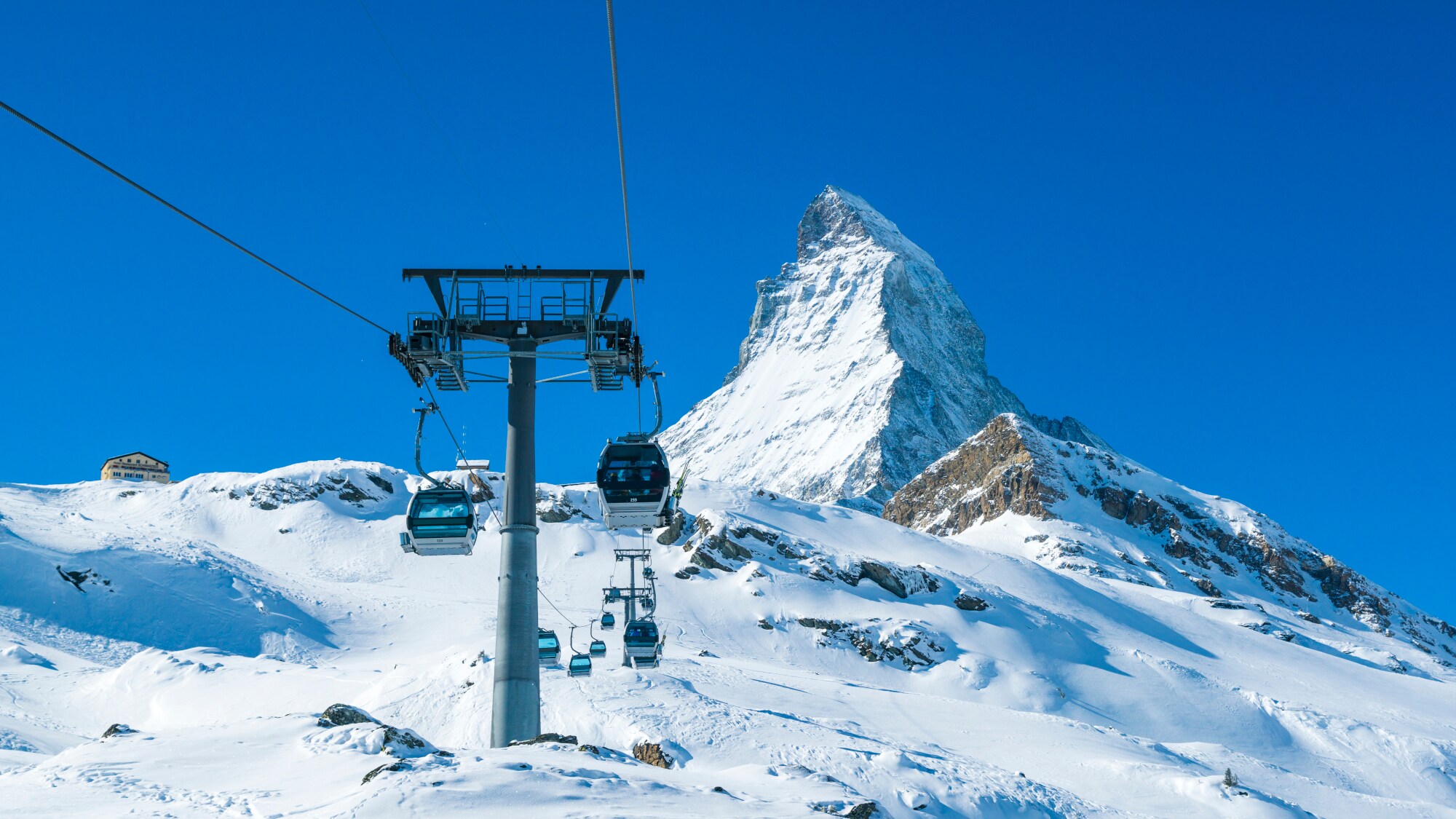 Berggondel mit schneebedeckter Piste, Matterhorn und blauem Himmel im Hintergrund.