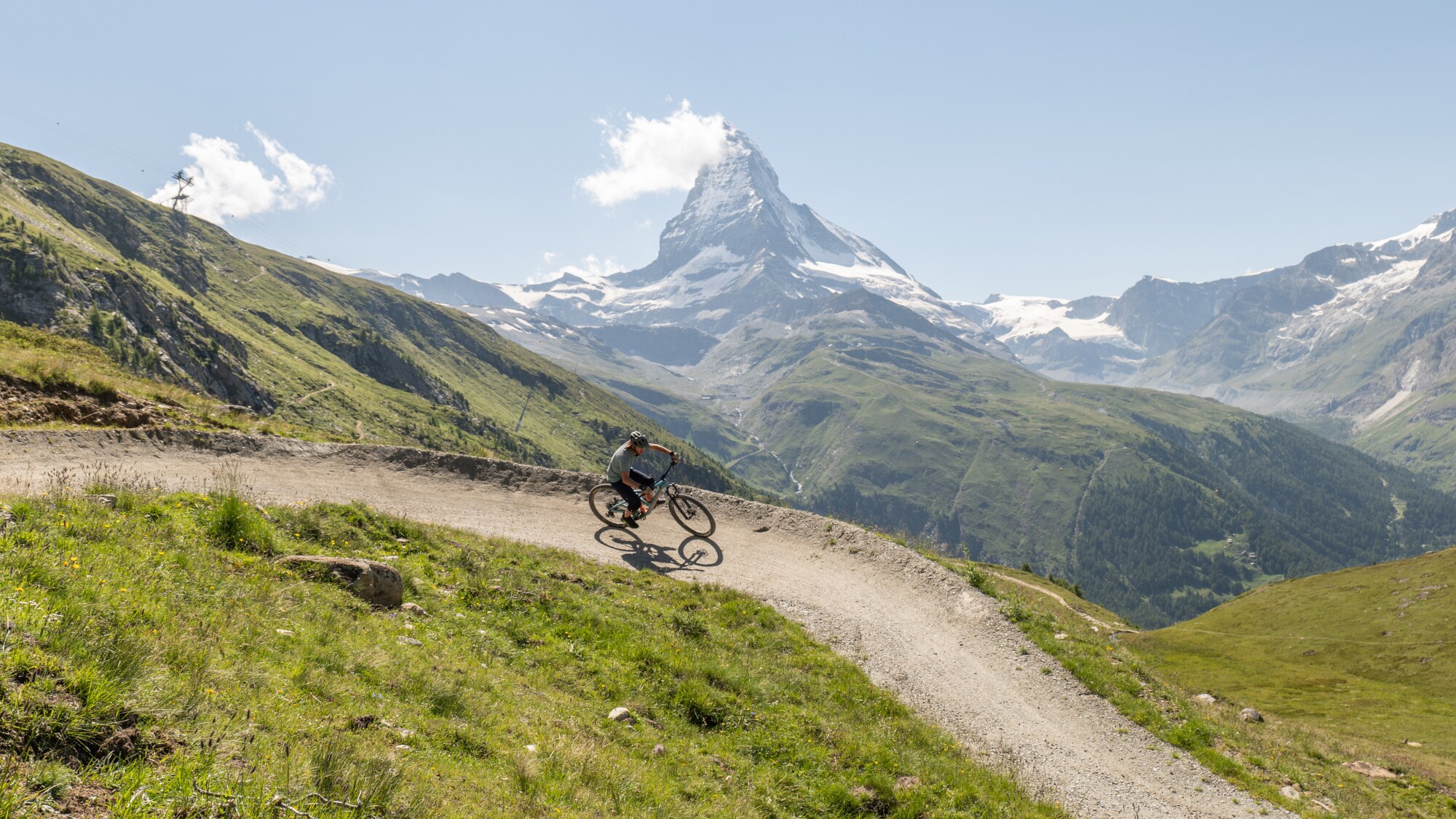 Eine Person mit Mountainbike in den sommerlichen Schweizer Alpen mit Matterhorn im Hintergrund.
