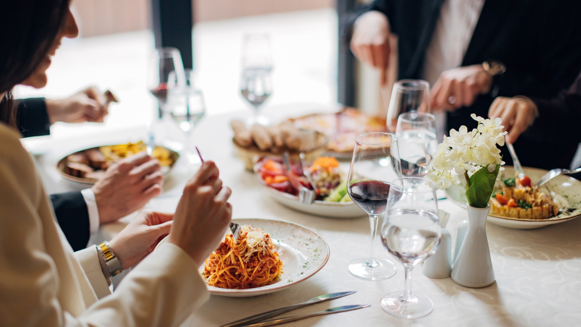 Eine Gruppe Personen an einem weiß eingedeckten Tisch in einem Restaurant mit verschiedenen Gerichten wie beispielsweise Pasta.