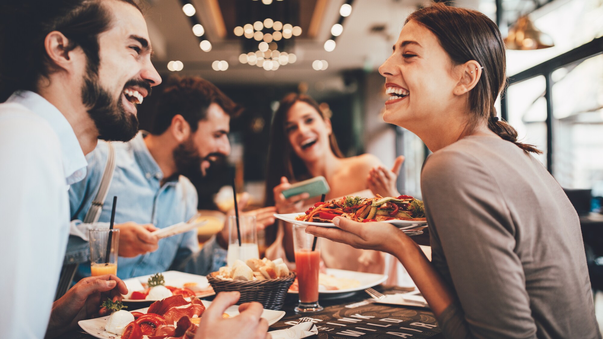Eine Gruppe fröhlicher Personen in einem Restaurant. Eine lachende Frau hält einen Teller in der Hand. Eine Gruppe fröhlicher Personen in einem Restaurant. Eine lachende Frau hält einen Teller in der Hand.