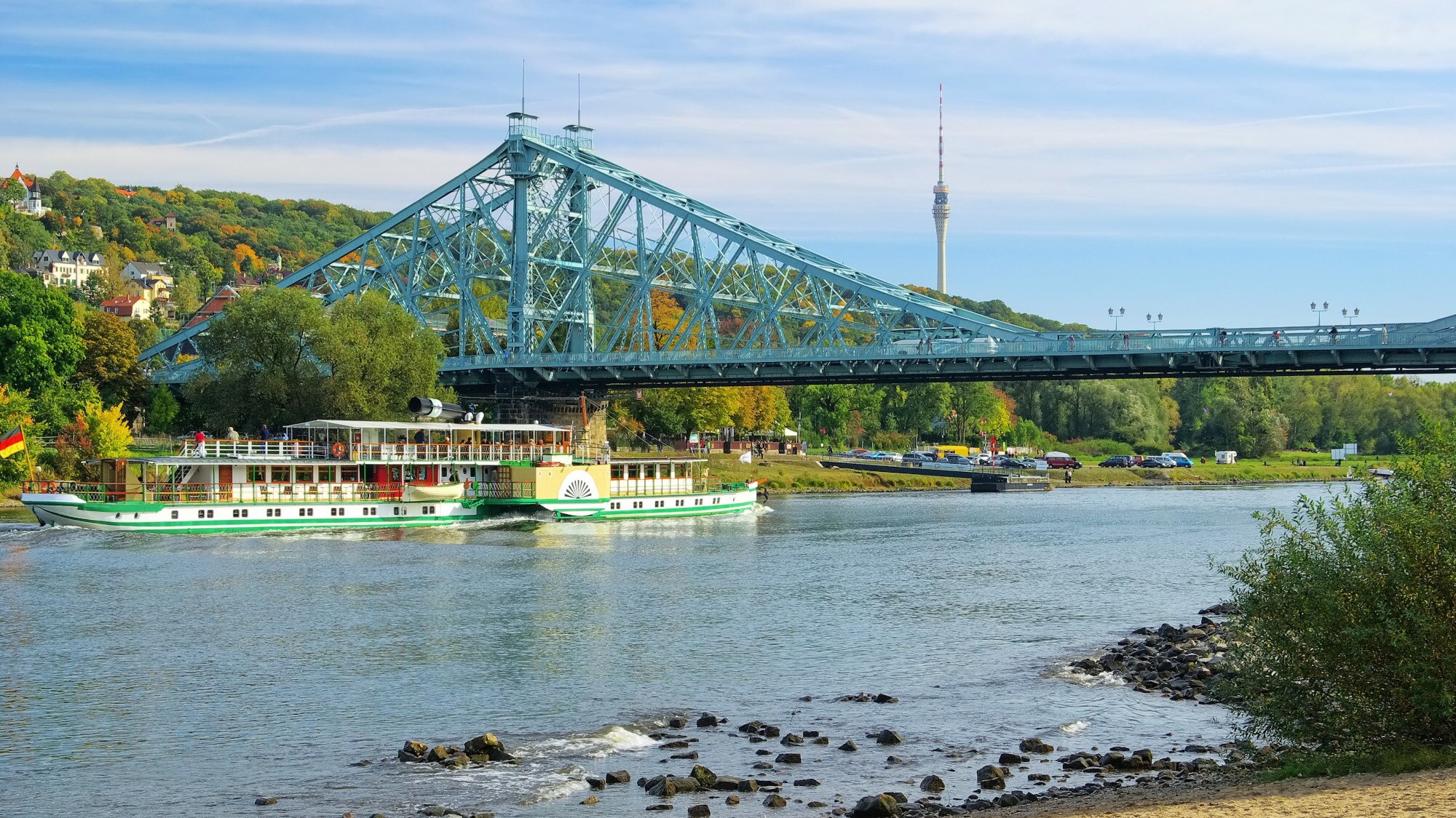 Blick vom Ufer auf das Blaue Wunder, unter dem ein Flussdampfer hindurchfährt.