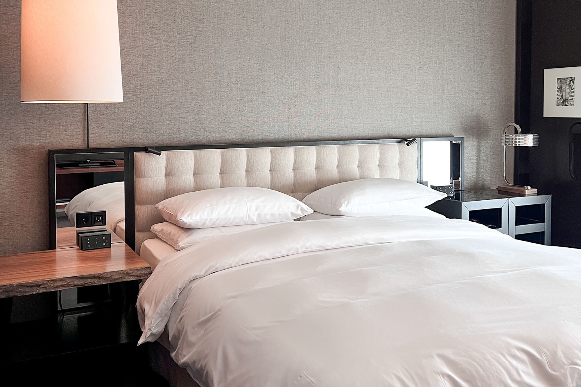 Doppelbett mit gepolstertem Kopfteil und Spiegeln sowie Nachttischen im modernen, minimalistischen Design vor einer grau tapezierten Wand.