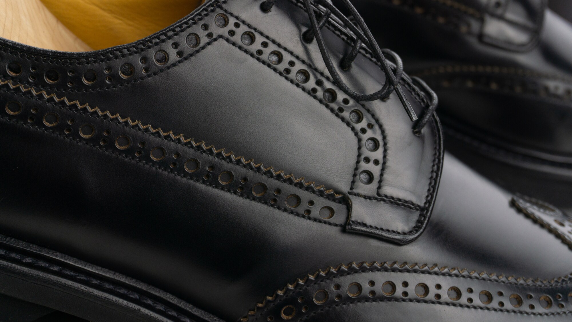 Nahaufnahme eines schwarzen Brogue Derby Schuhs mit Schnürsenkeln, Lochmuster und Derbybogen.