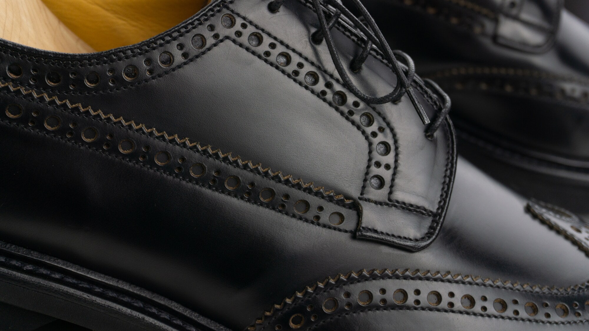 Nahaufnahme eines schwarzen Brogue Derby Schuhs mit Schnürsenkeln, Lochmuster und Derbybogen. Nahaufnahme eines schwarzen Brogue Derby Schuhs mit Schnürsenkeln, Lochmuster und Derbybogen.