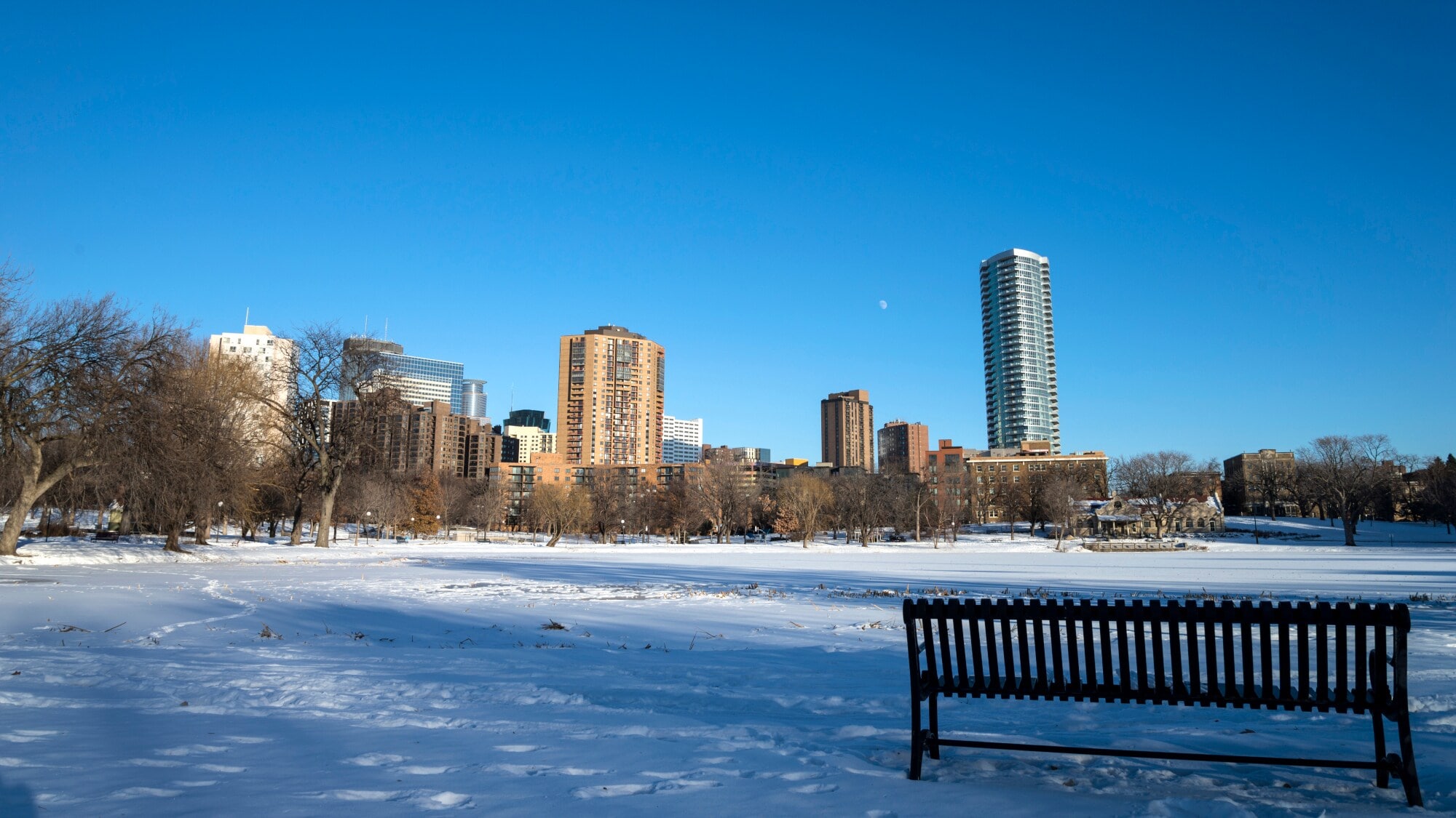 Eine Sitzbank in einem Park in Minneapolis im Winter. Im Hintergrund die Skyline der Stadt bei Sonnenschein. Eine Sitzbank in einem Park in Minneapolis im Winter. Im Hintergrund die Skyline der Stadt bei Sonnenschein.