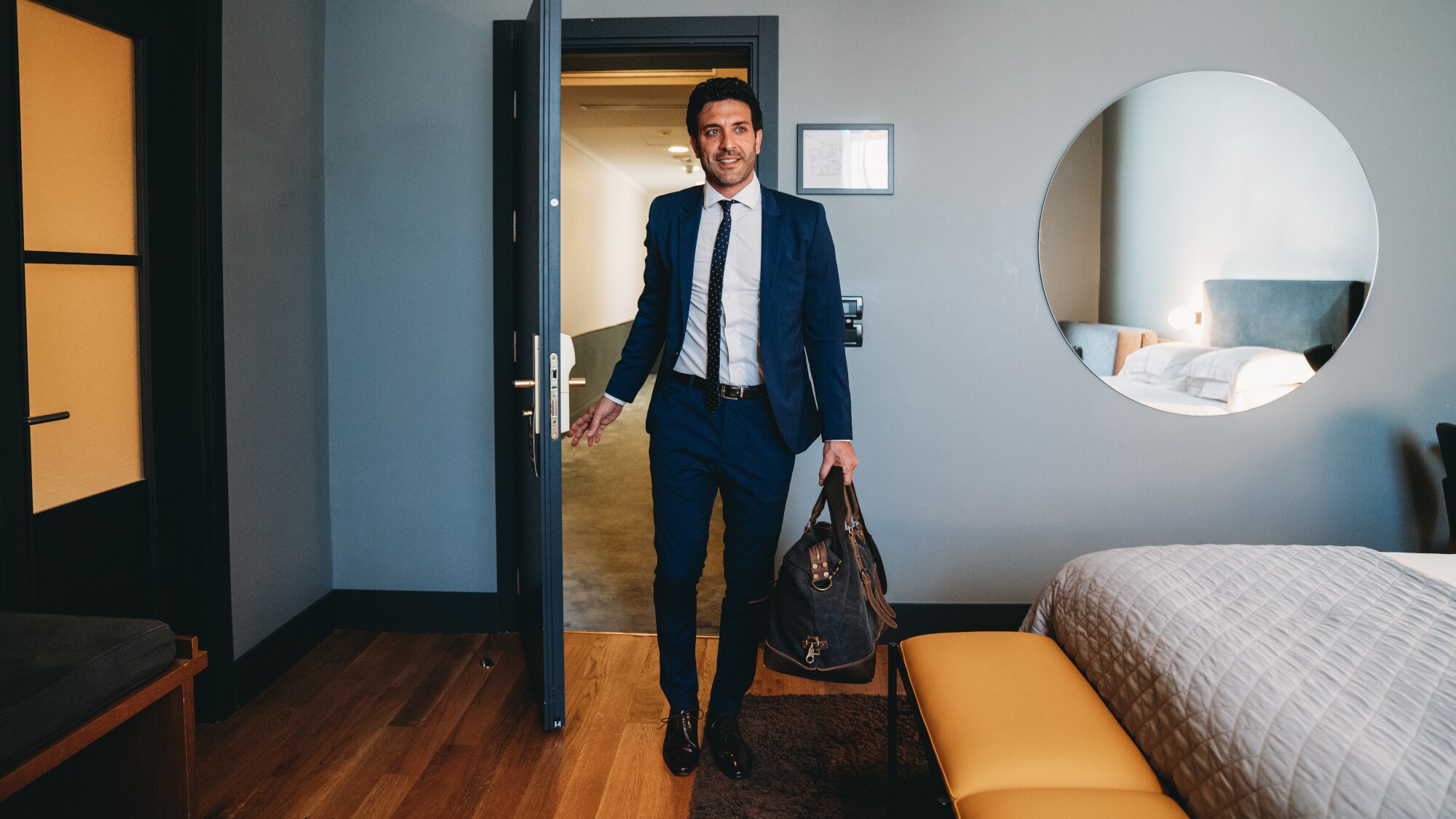 Ein Mann im Anzug trägt eine Reisetasche und betritt ein Hotelzimmer.