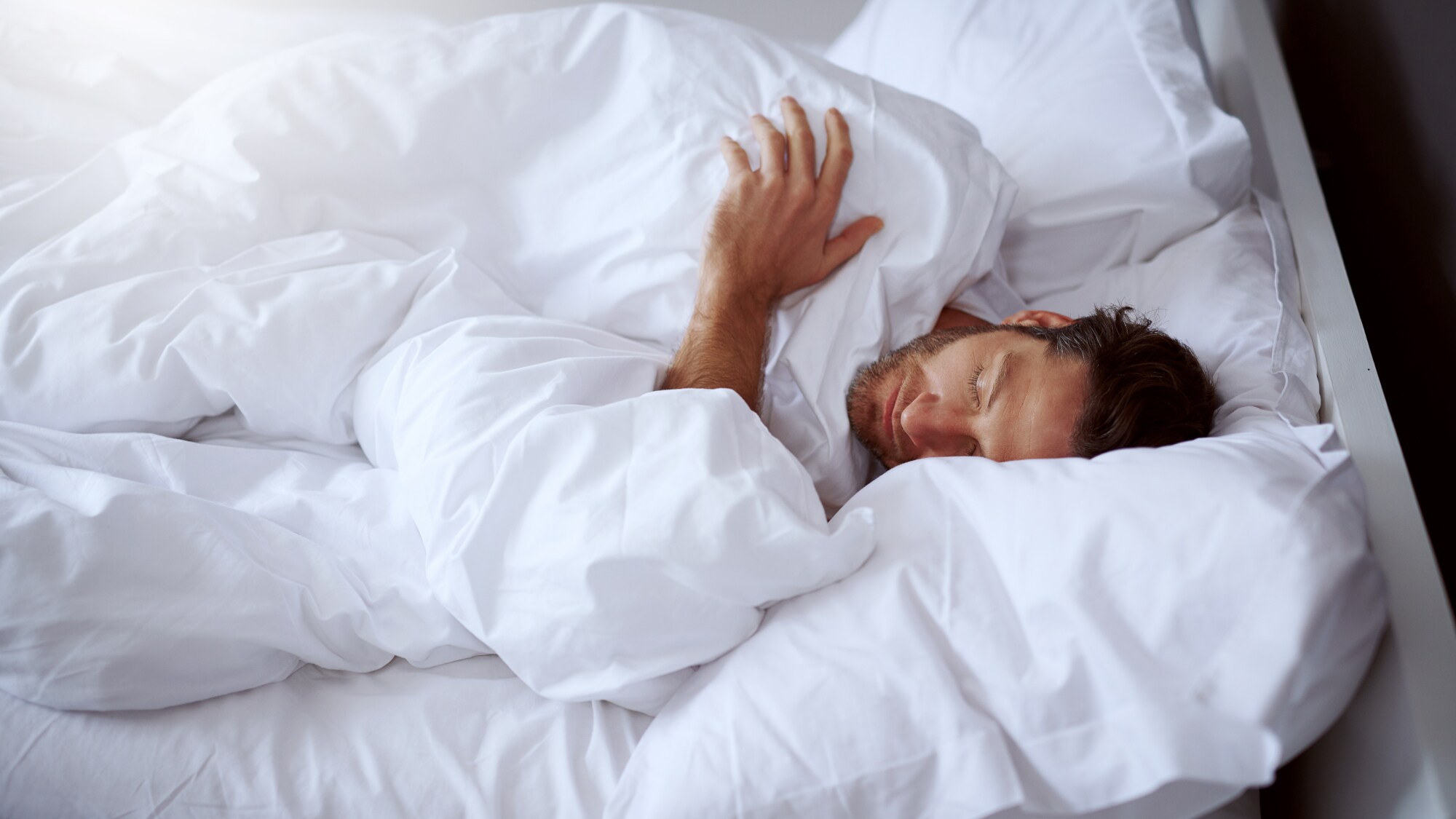 Ein Mann, der in einem Bett mit weißer Bettwäsche und Laken schläft. Ein Mann, der in einem Bett mit weißer Bettwäsche und Laken schläft.