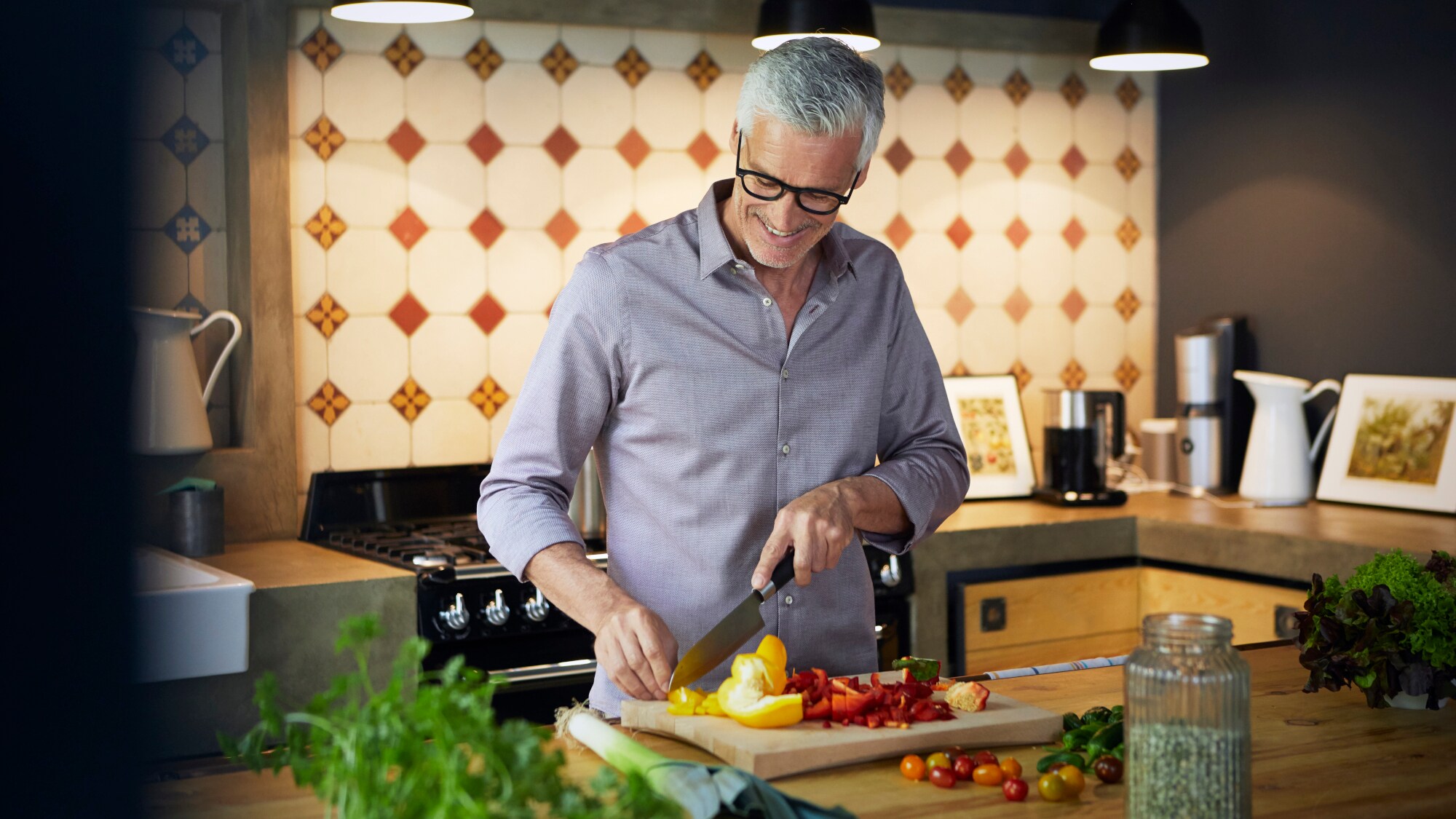 Ein lächelnder älterer Mann, der in einer Küche auf einem Küchenbrett eine Paprika schneidet. Ein lächelnder älterer Mann, der in einer Küche auf einem Küchenbrett eine Paprika schneidet.