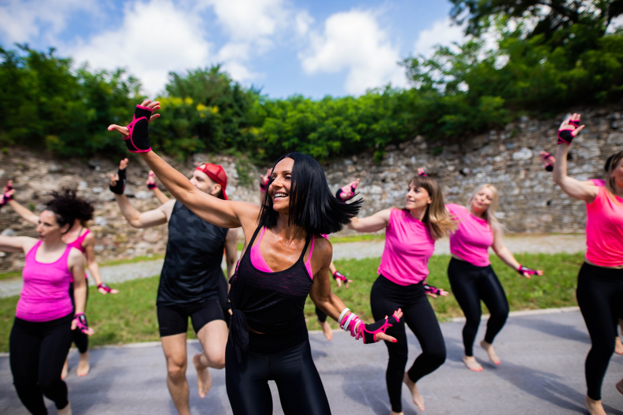 Mehrere Personen unter freiem Himmel heben synchron einen Arm, blicken in dieselbe Richtung und knicken das gegenüberliegende Bein ein.