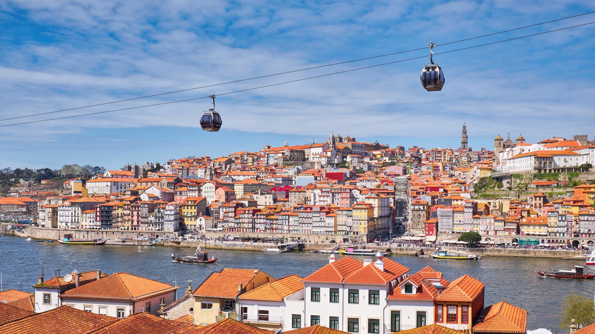 Eine Seilbahn führt über das Douro-Ufer in Porto. Im Hintergrund liegen auf einem Hügel viele bunte Häuser der Altstadt. Eine Seilbahn führt über das Douro-Ufer in Porto. Im Hintergrund liegen auf einem Hügel viele bunte Häuser der Altstadt.