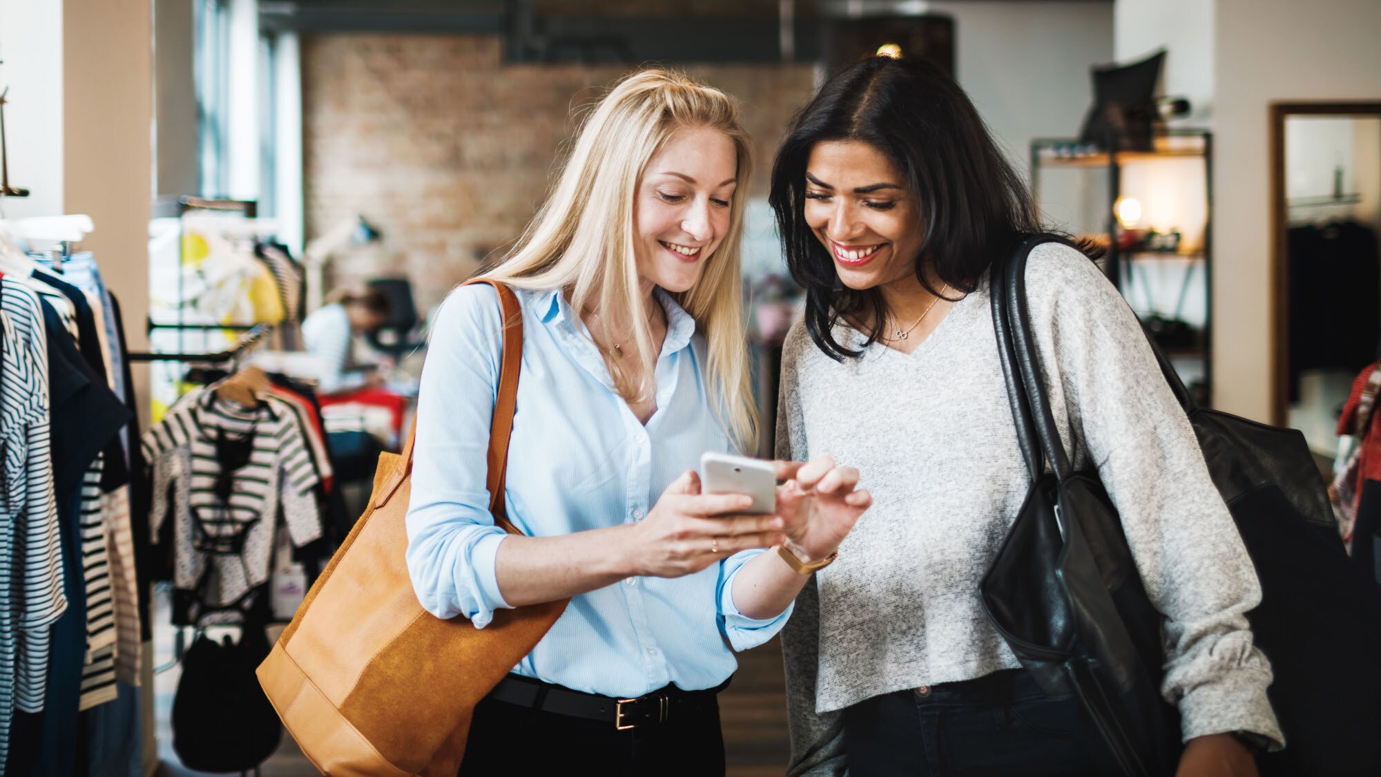 Zwei Frauen schauen gemeinsam auf ein Smartphone in einer Modeboutique. Zwei Frauen schauen gemeinsam auf ein Smartphone in einer Modeboutique.