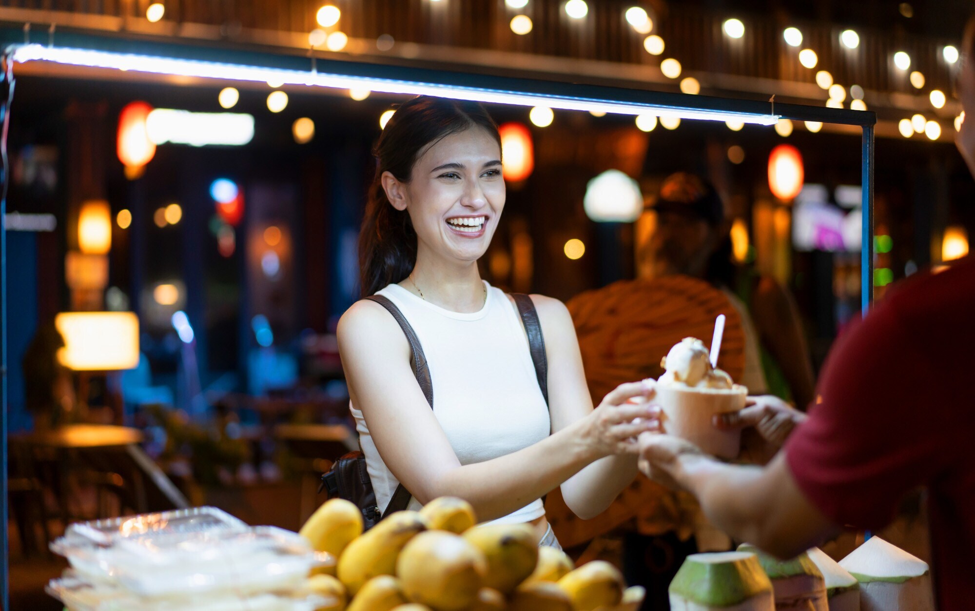 Eine junge Frau kauft Streetfood an einem erleuchteten Marktstand bei Nacht. Eine junge Frau kauft Streetfood an einem erleuchteten Marktstand bei Nacht.