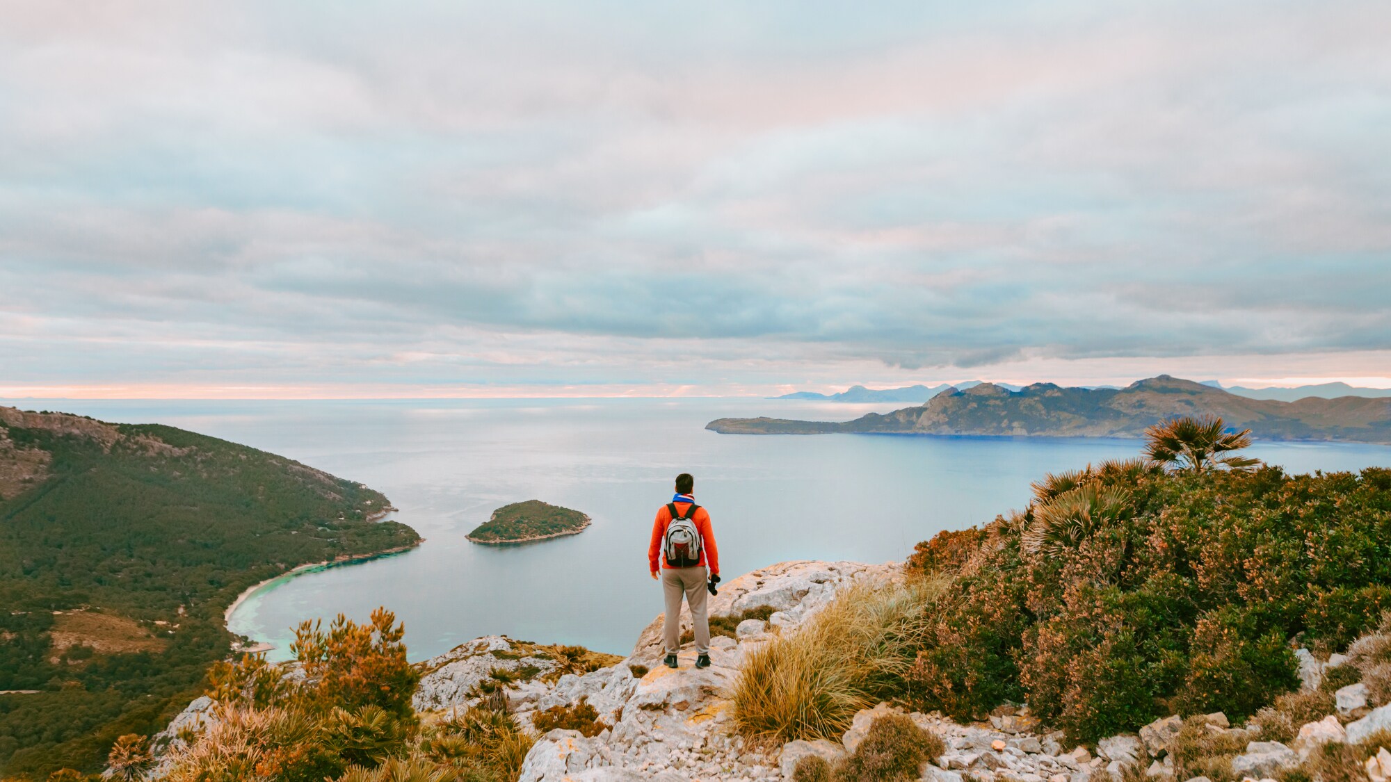Rückenansicht eines Wanderers auf Mallorca, der an einer Klippe steht und auf das Meer im Hintergrund blickt. Rückenansicht eines Wanderers auf Mallorca, der an einer Klippe steht und auf das Meer im Hintergrund blickt.
