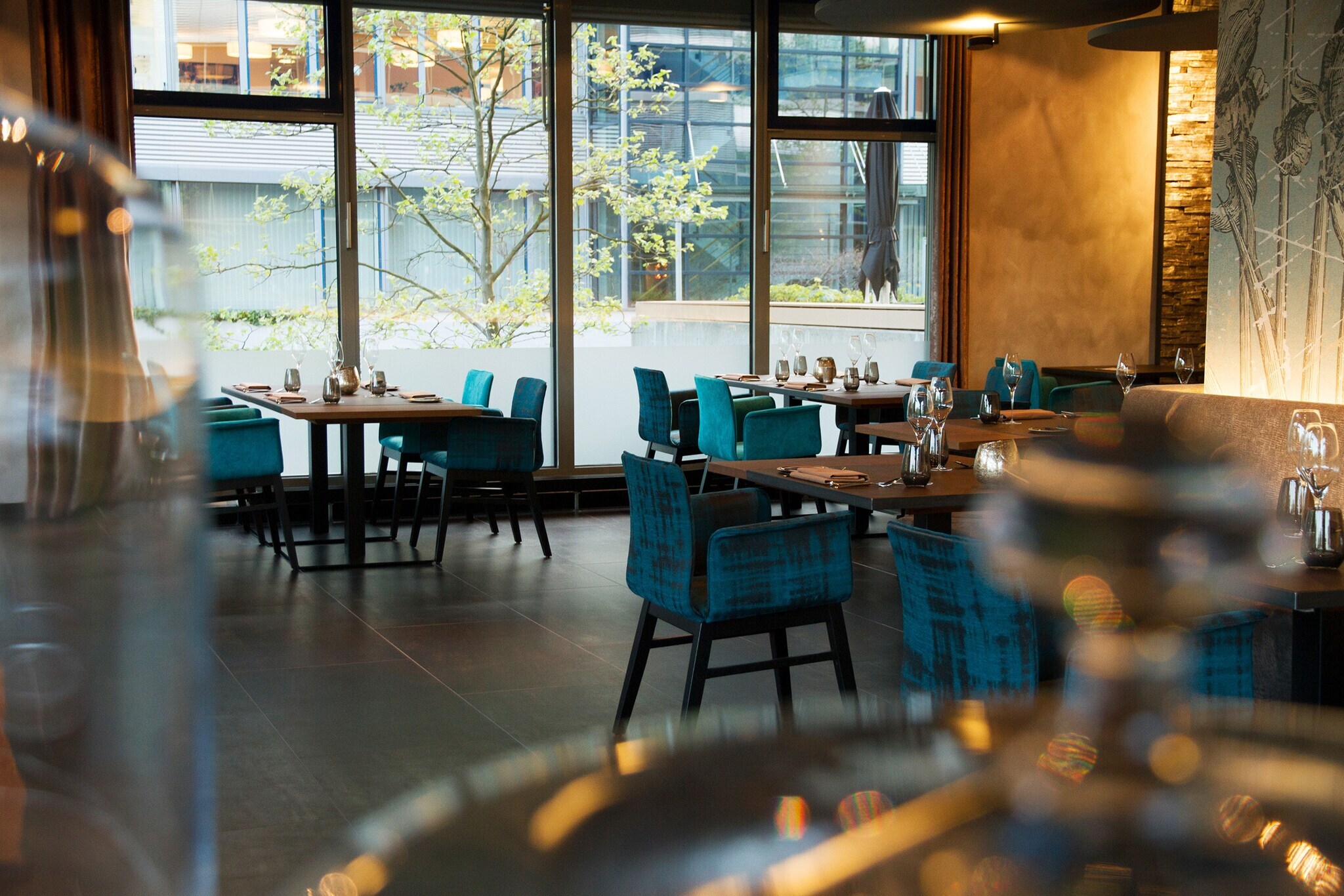 Blaue Polsterstühle an eingedeckten Tischen im Speisesaal eines Restaurants mit bodentiefen Fenstern.