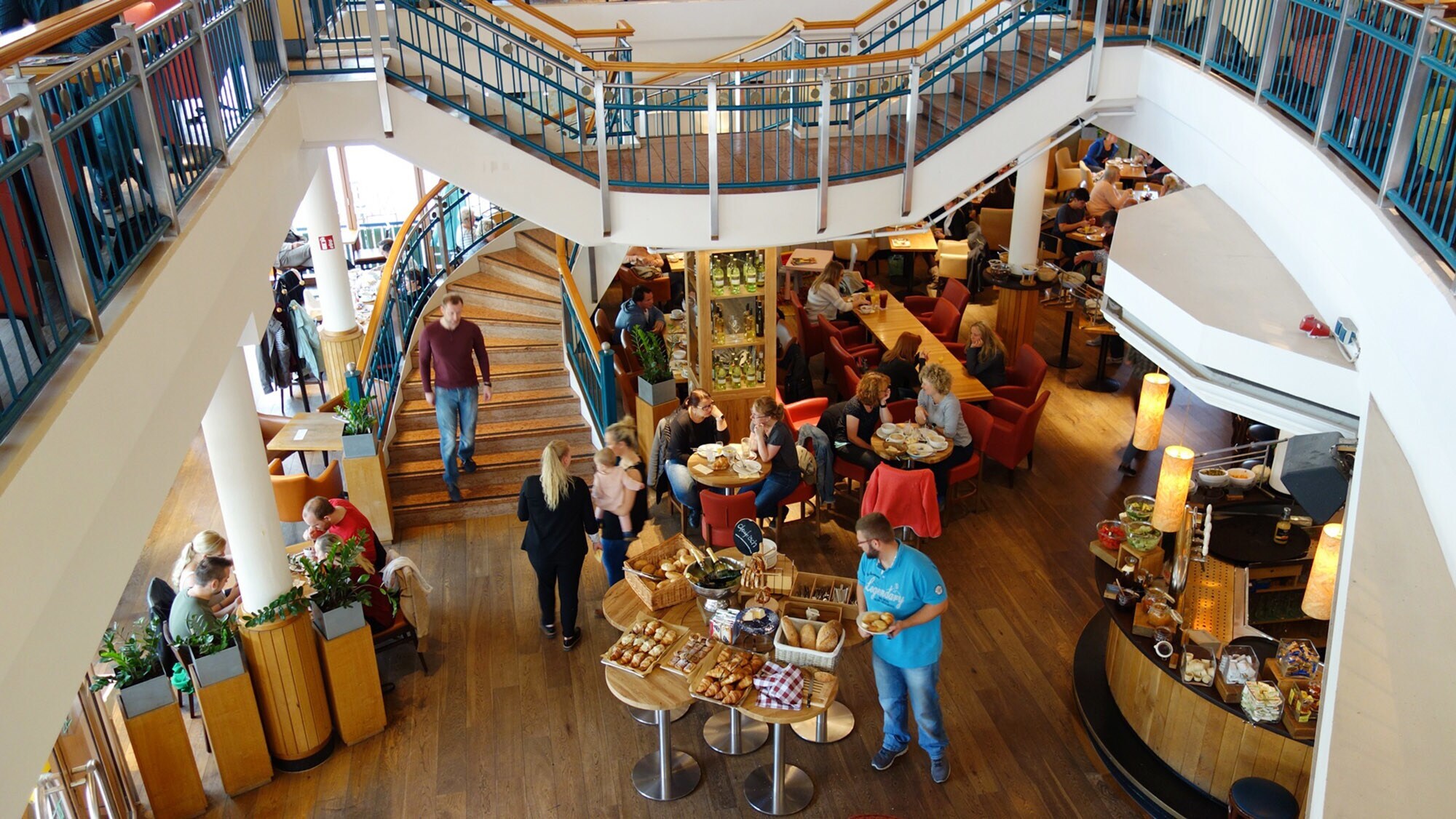 Aufsicht eines Innenraums in einem belebten Bistro mit Frühstücksbuffet.