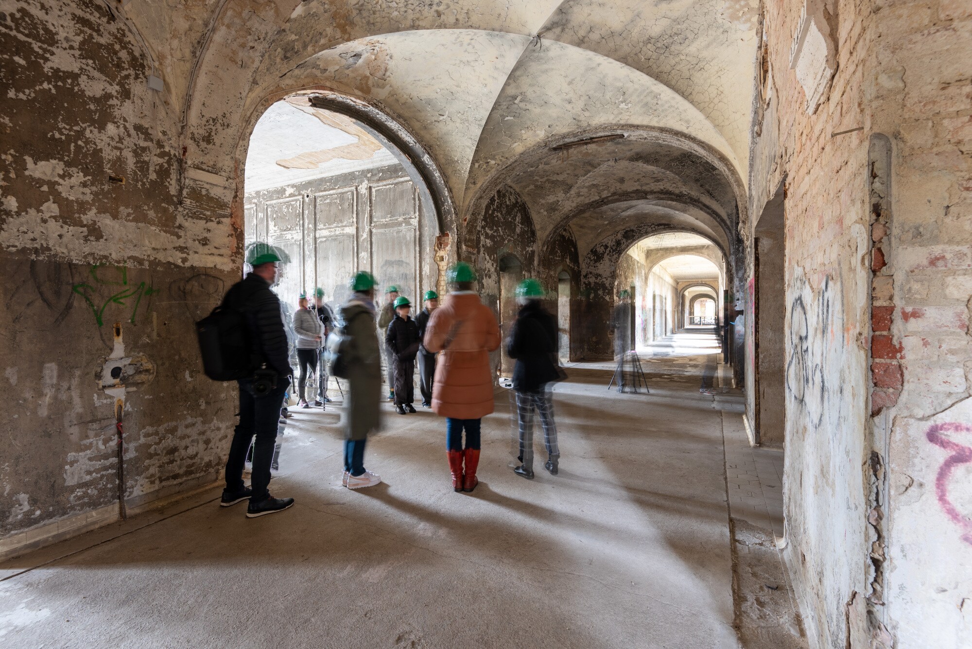 Besuchergruppe mit grünen Bauhelmen in einem alten Gewölbegang.