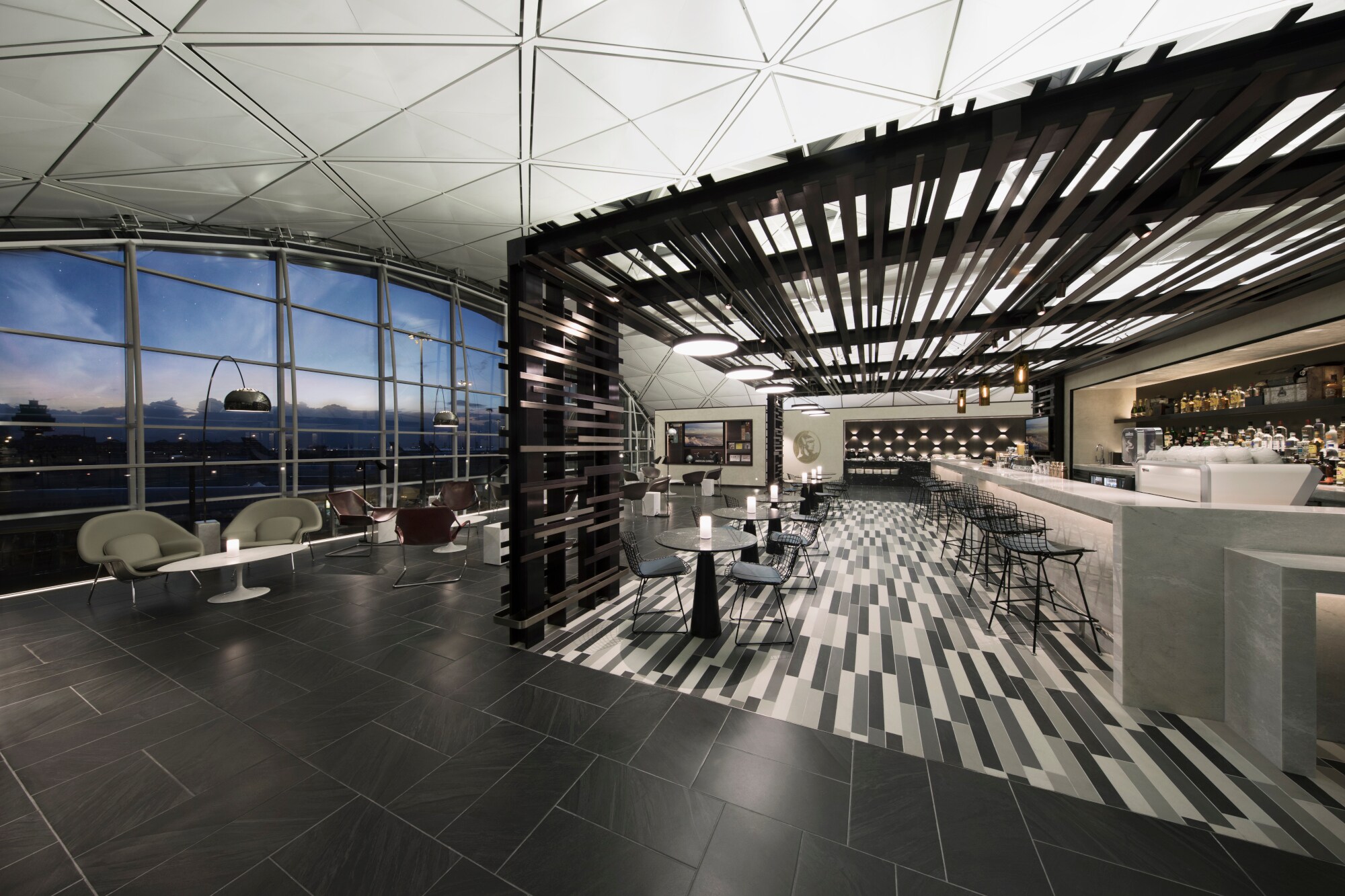 Moderne Flughafenlounge mit Barbereich und Blick aufs Rollfeld durch Panoramafenster bei Nacht.