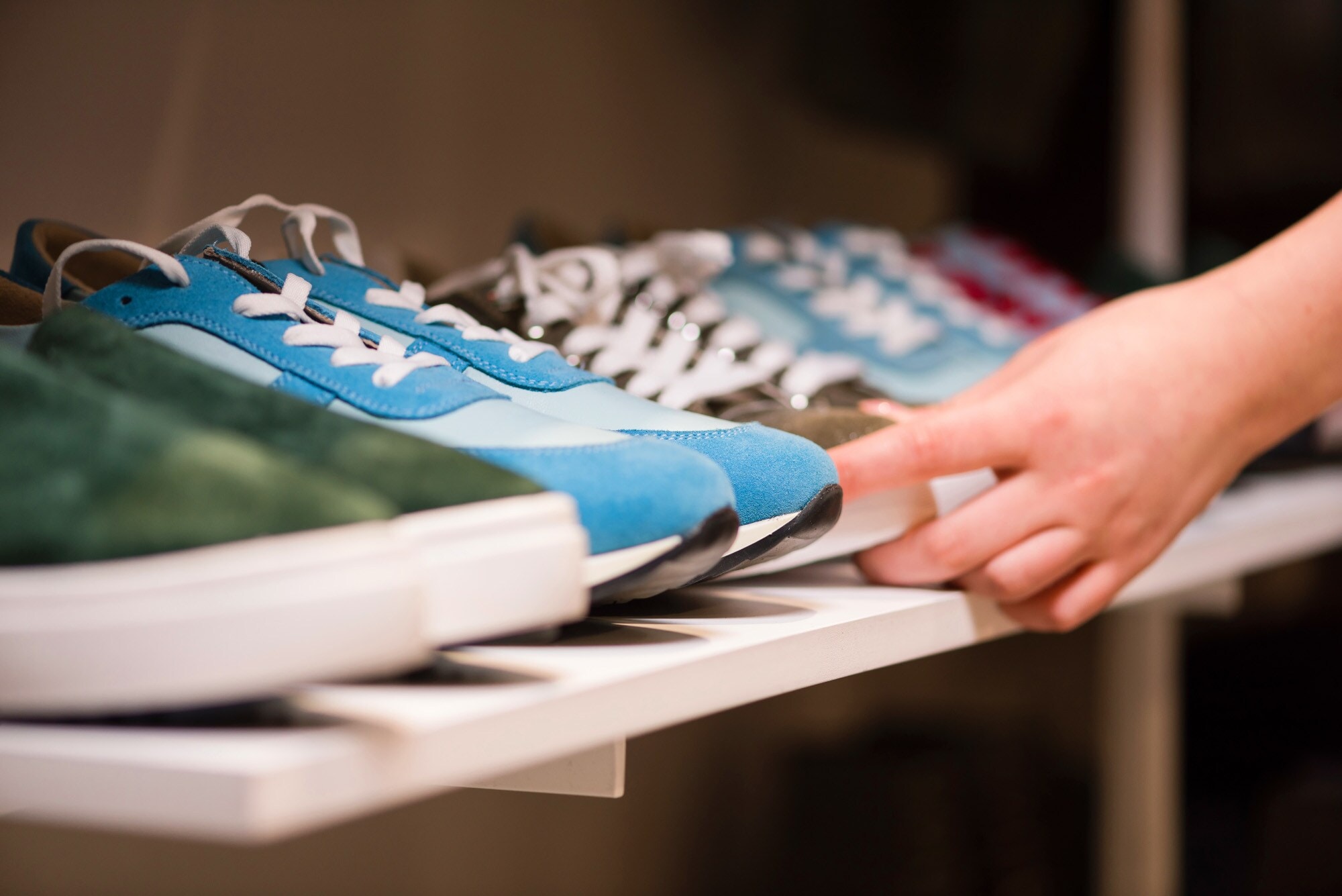 Eine Hand greift nach einem Sneaker aus einer Reihe von Turnschuhen in einem Regal. Eine Hand greift nach einem Sneaker aus einer Reihe von Turnschuhen in einem Regal.