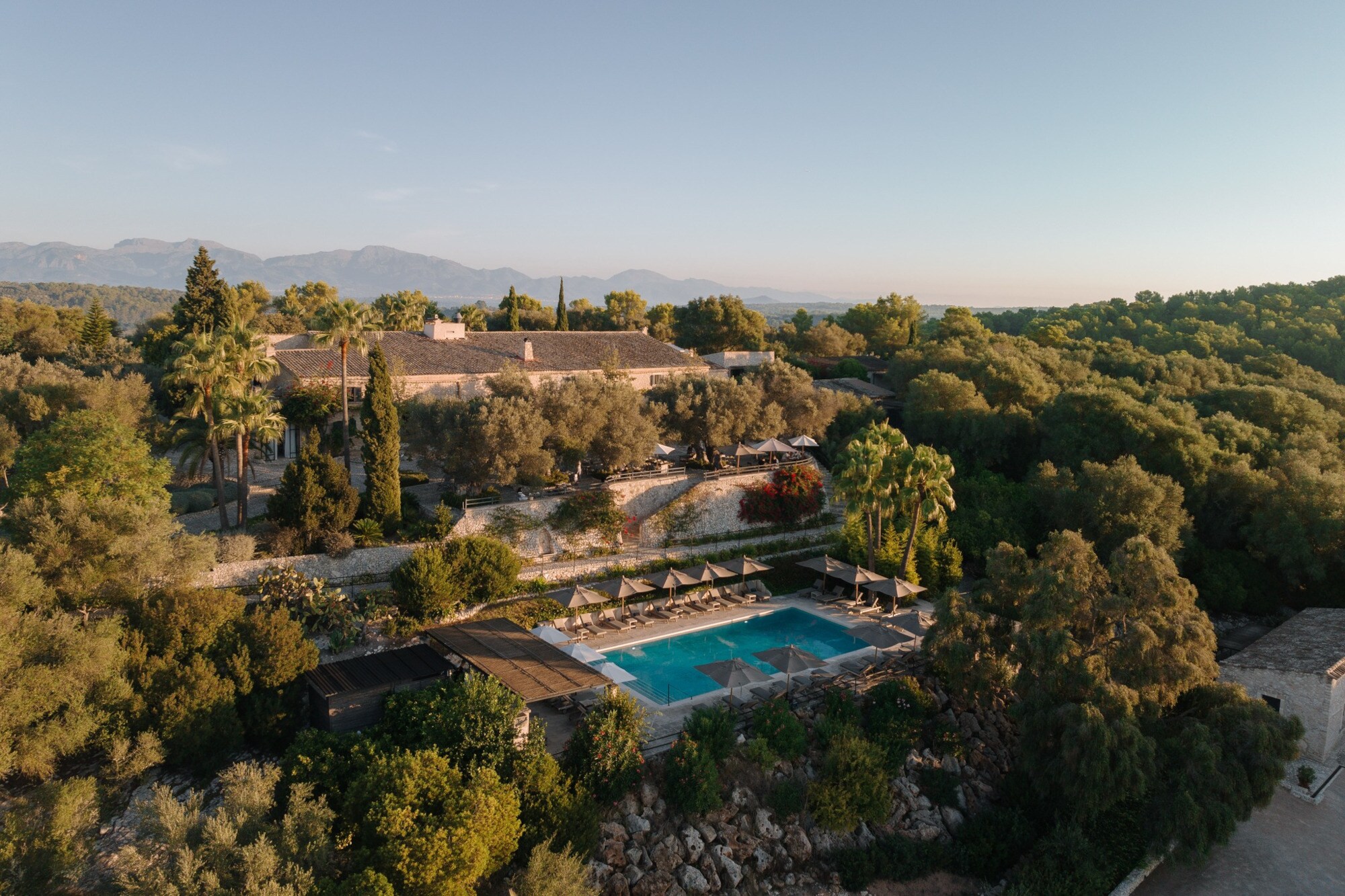Luftaufnahme einer Finca mit Pool inmitten einer bewaldeten Hügellandschaft.