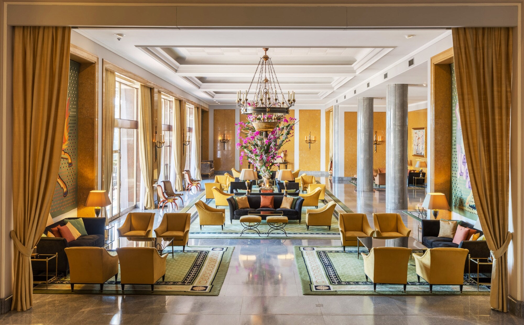 Ein elegantes Hotelfoyer mit Marmorsäulen und gelben Sesseln, in der Mitte ein großes Blumenbouquet. Ein elegantes Hotelfoyer mit Marmorsäulen und gelben Sesseln, in der Mitte ein großes Blumenbouquet.