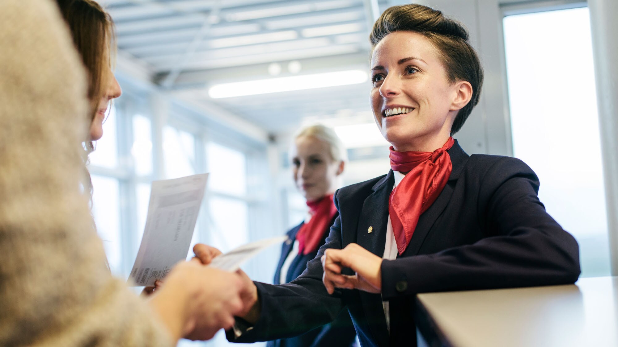 Eine Flugbegleiterin checkt Boardingpässe und begrüßt Reisende am Gate.
