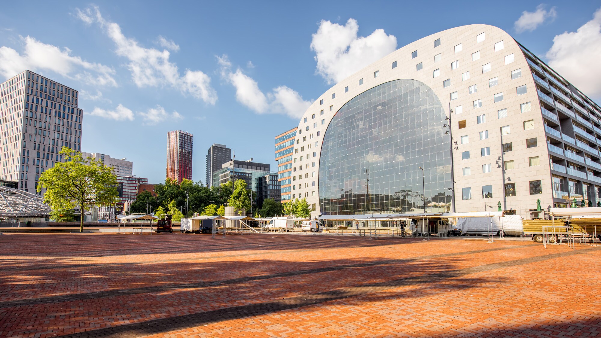 Blick von oben auf eine Stadt mit einer grünen Wiese, Hochhäusern und einer modernen, hufeisenförmigen Markthalle. Blick von oben auf eine Stadt mit einer grünen Wiese, Hochhäusern und einer modernen, hufeisenförmigen Markthalle.