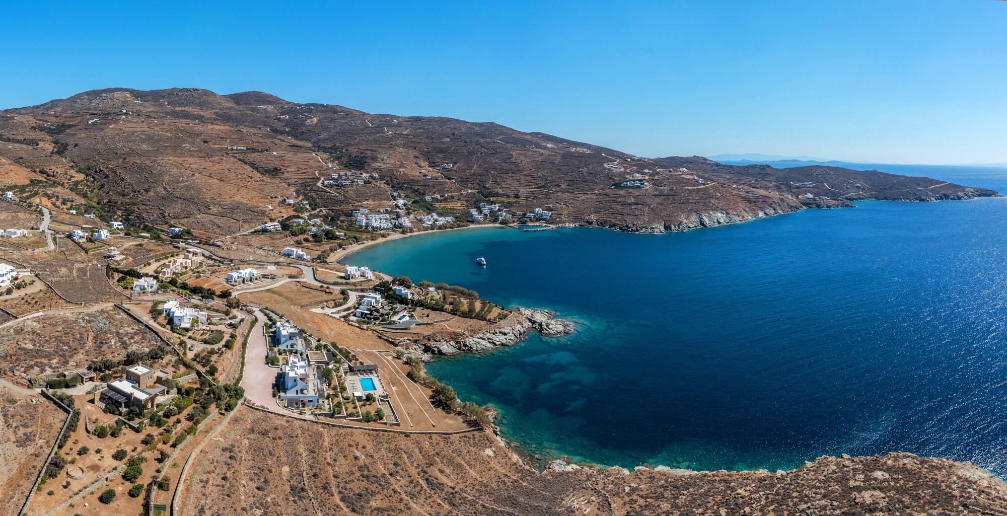 Karge Insellandschaft mit Ortschaft aus weißen Häusern an einer Meeresbucht mit Sandstrand.