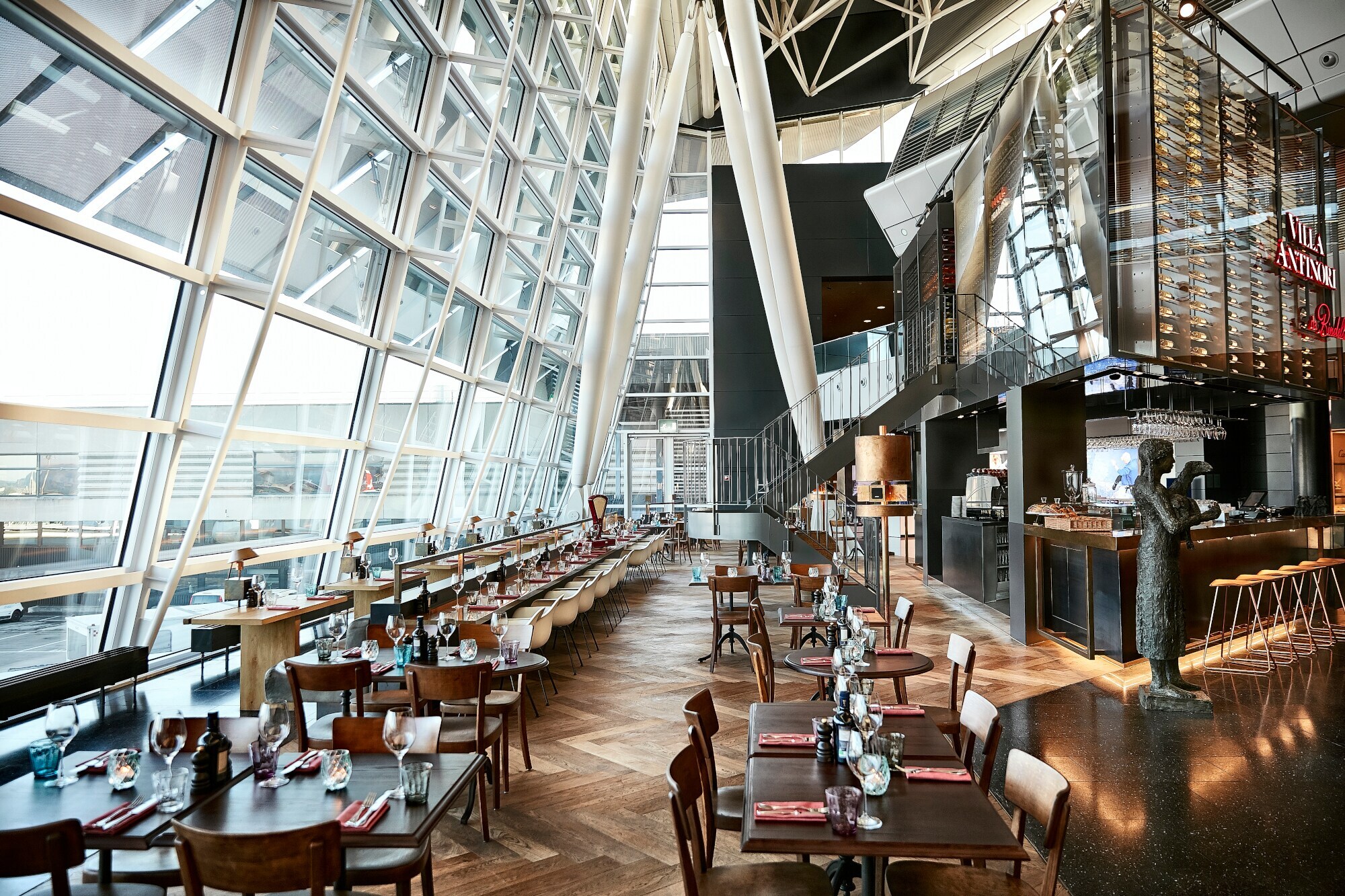 Eingedeckte Esstische eines stilvollen Restaurants mit Panoramafenstern in einem Flughafenterminal.