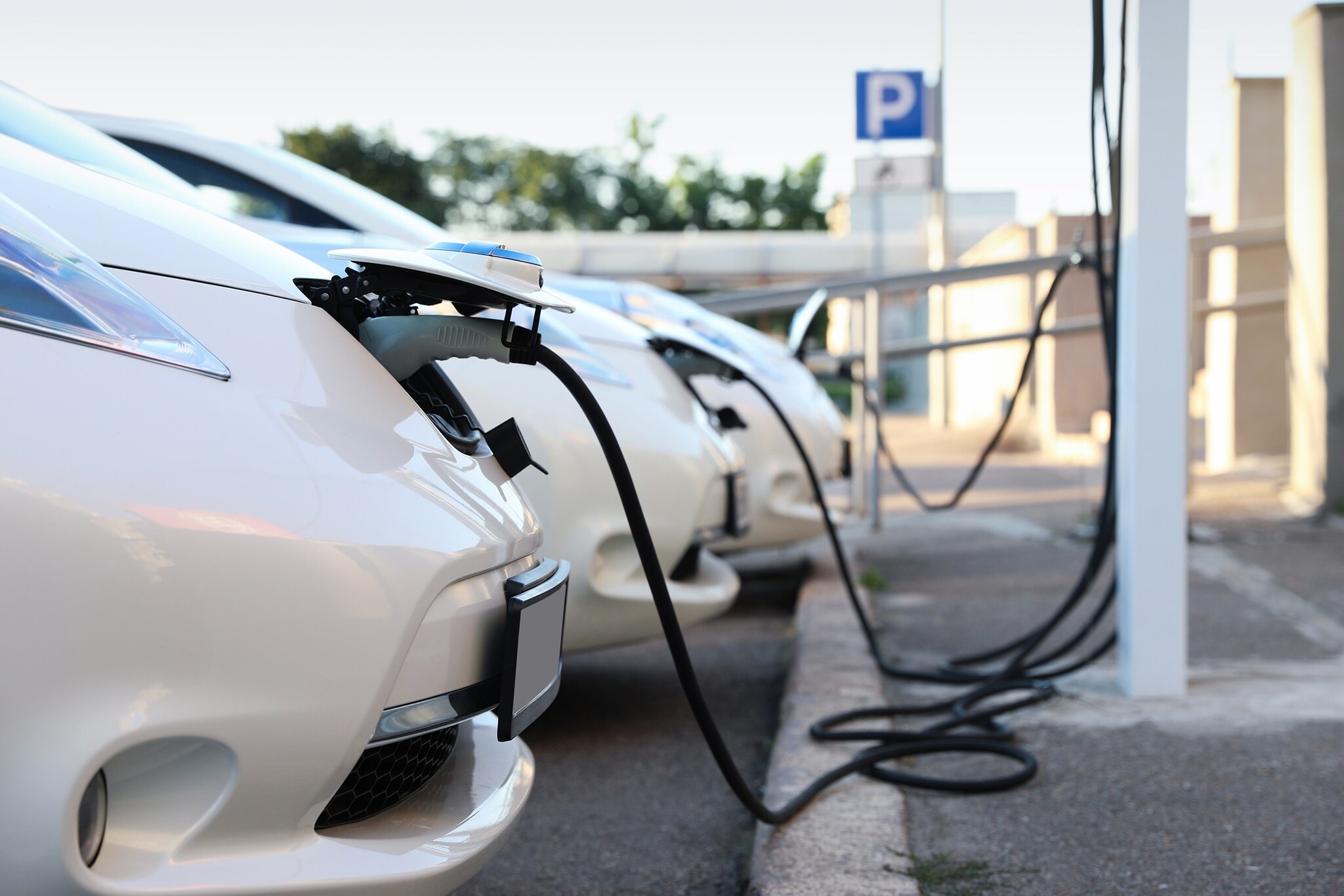Elektroautos im Fuhrpark: Diese Benefits warten auf dich Drei weiße Elektroautos werden an Ladesäulen aufgeladen.