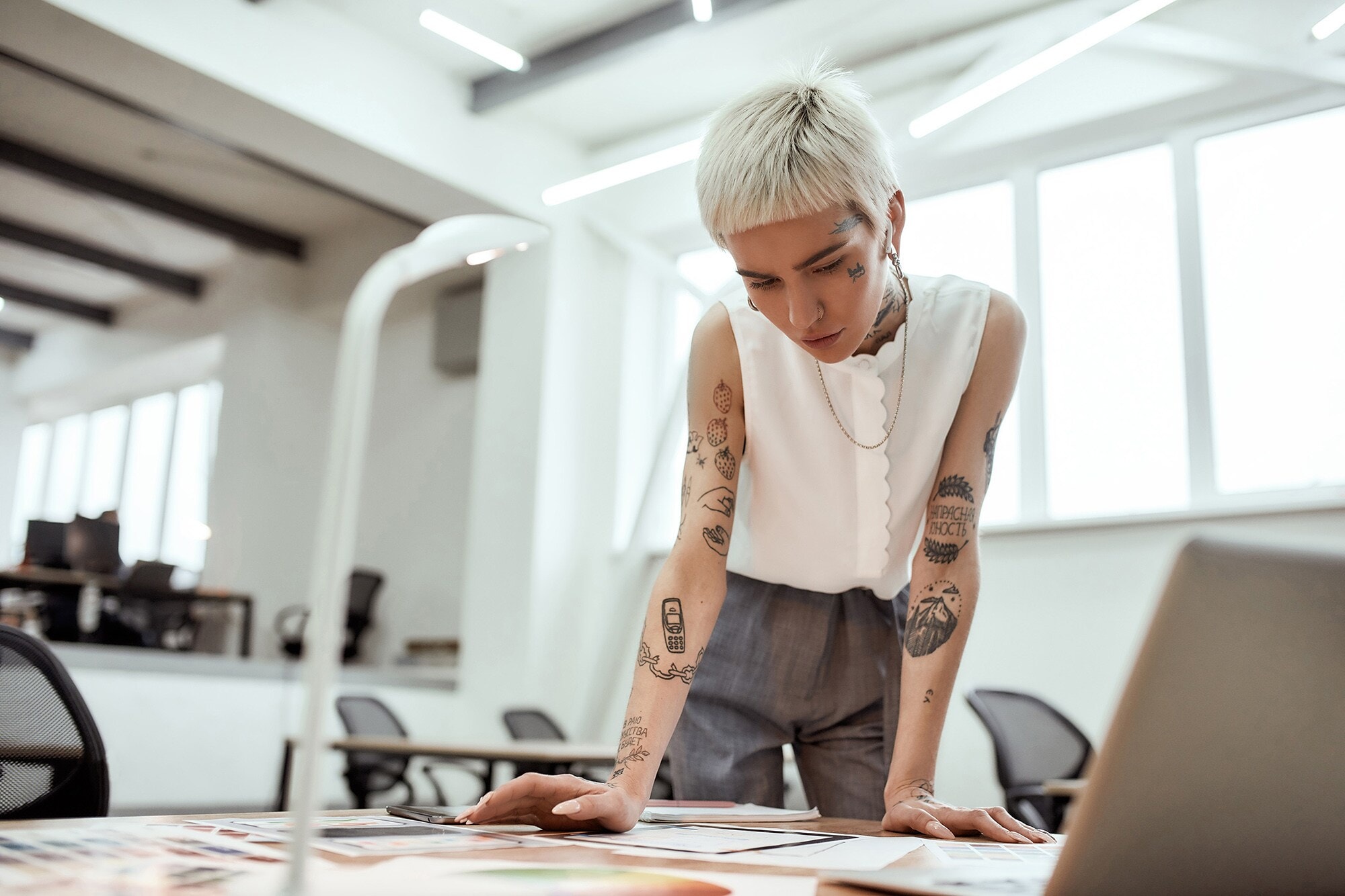 Brandbook Basics: Schritt für Schritt Eine junge tätowierte Frau steht am Schreibtisch und blickt auf verschiedene Entwürfe.