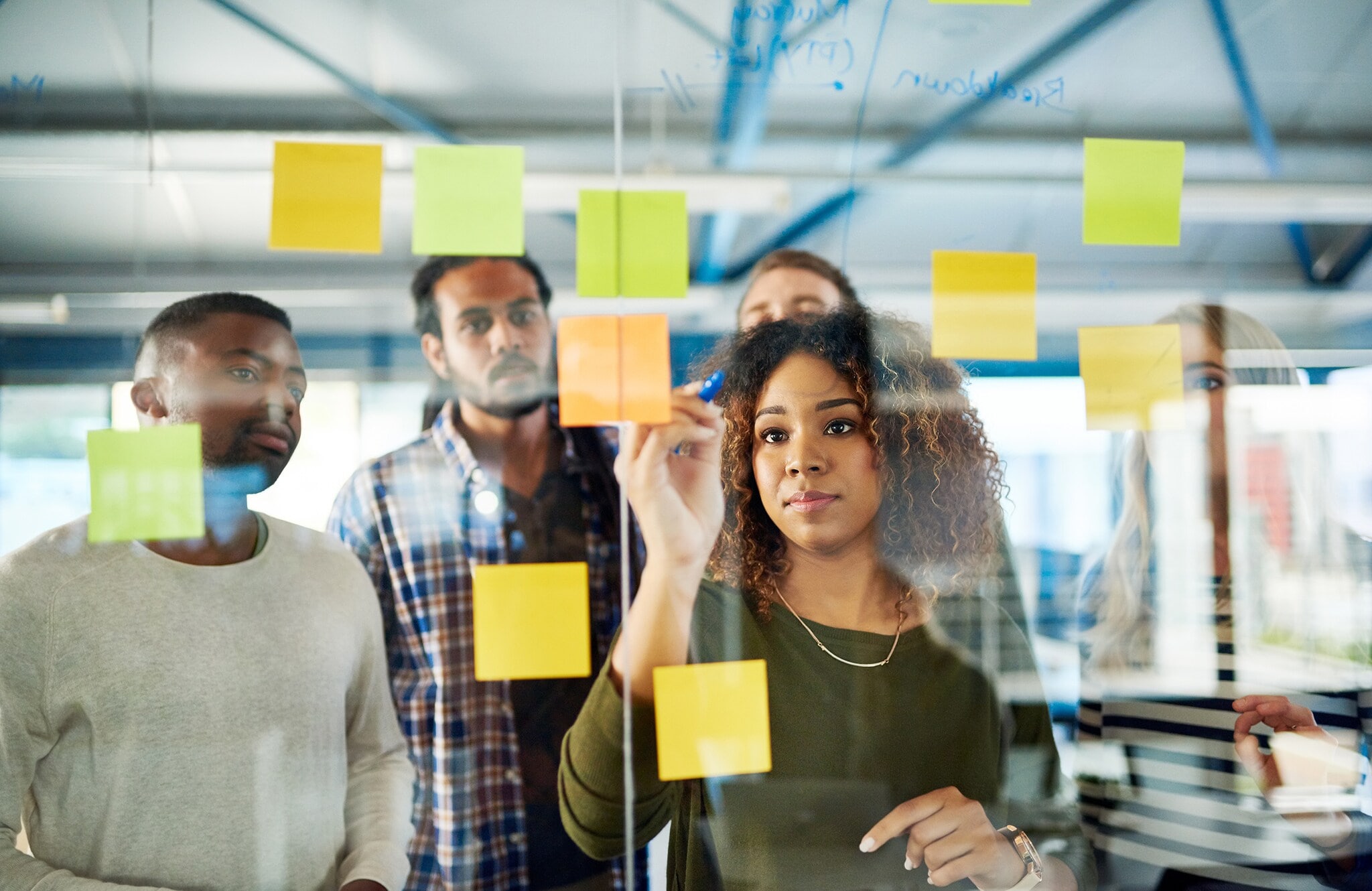 Perfect Match: So findest du den idealen Namen für dein Business Eine Gruppe Angestellter im Büro hinter einer Glaswand mit Klebezetteln.