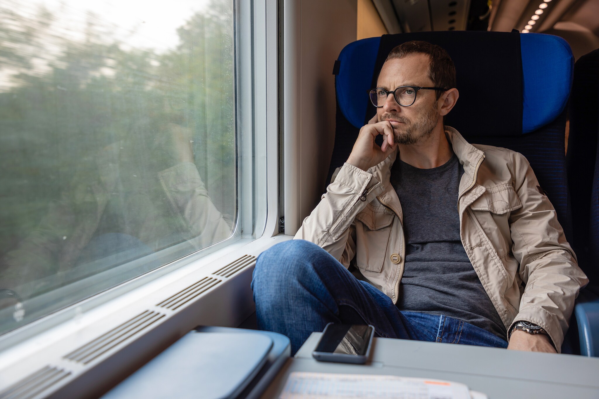 Ein Mann sitzt in fahrendem Zug und schaut aus dem Fenster.