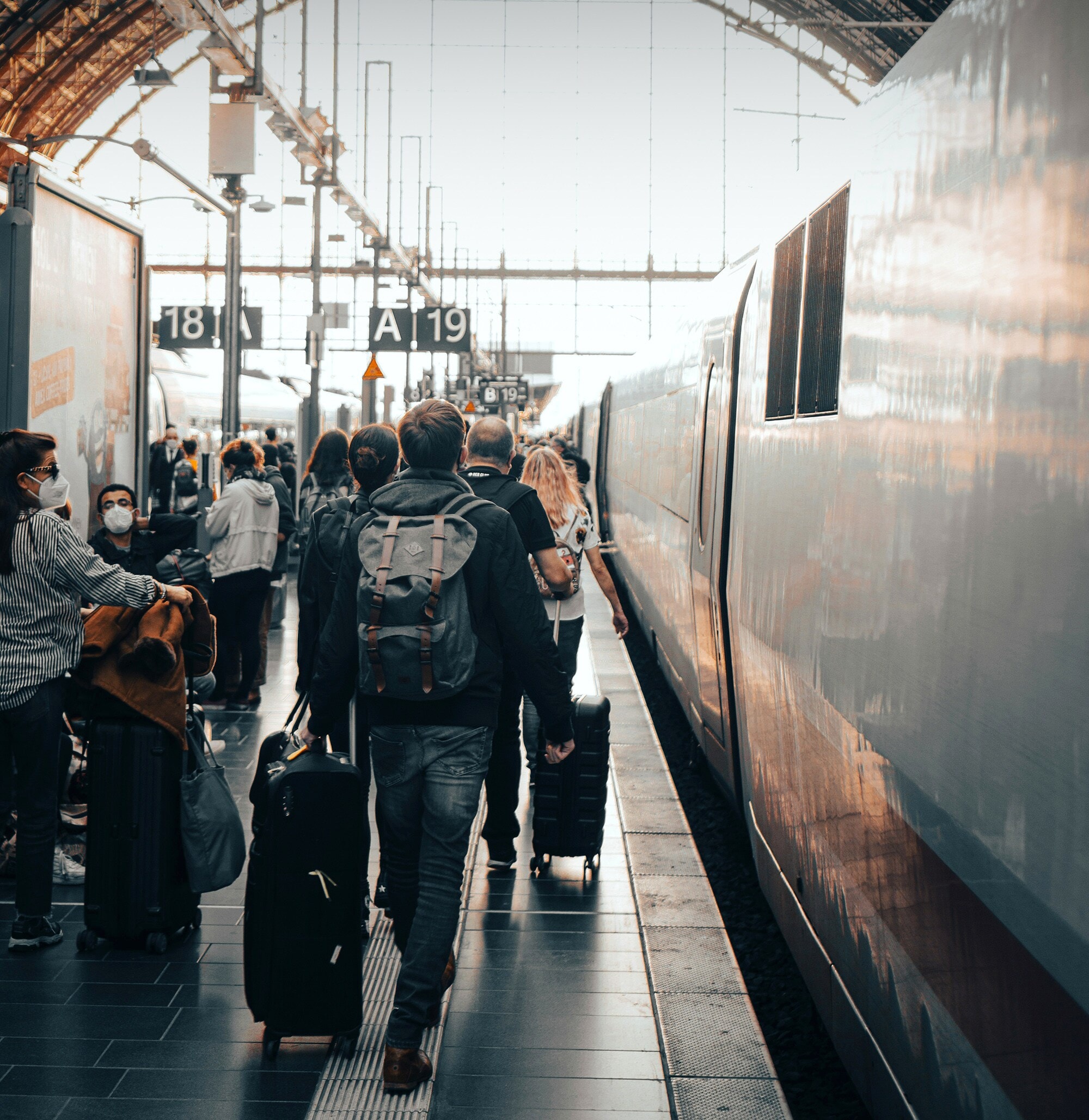 Reisende mit Gepäck laufen am Gleis in einem großen Bahnhof.