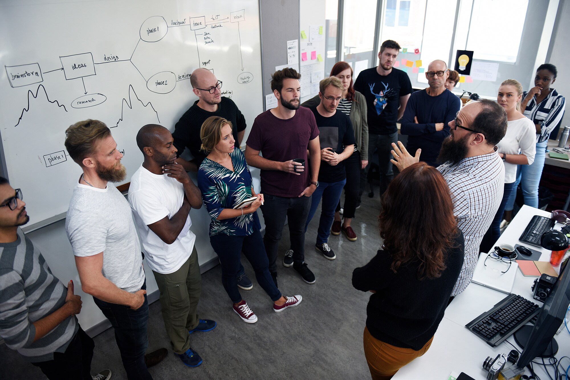 Ein diverses Business Team diskutiert miteinander vor einer Tafel.