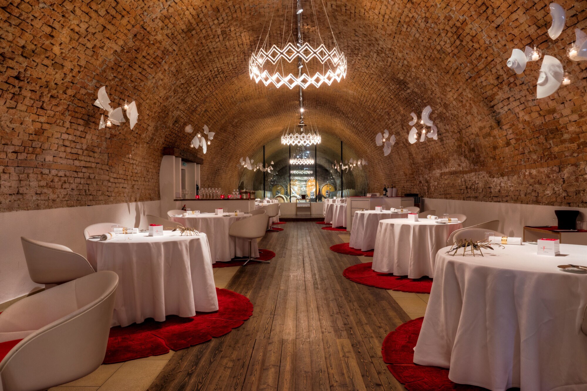 Speisesaal mit weiß eingedeckten, runden Tischen in einem Ziegelgewölbekeller.