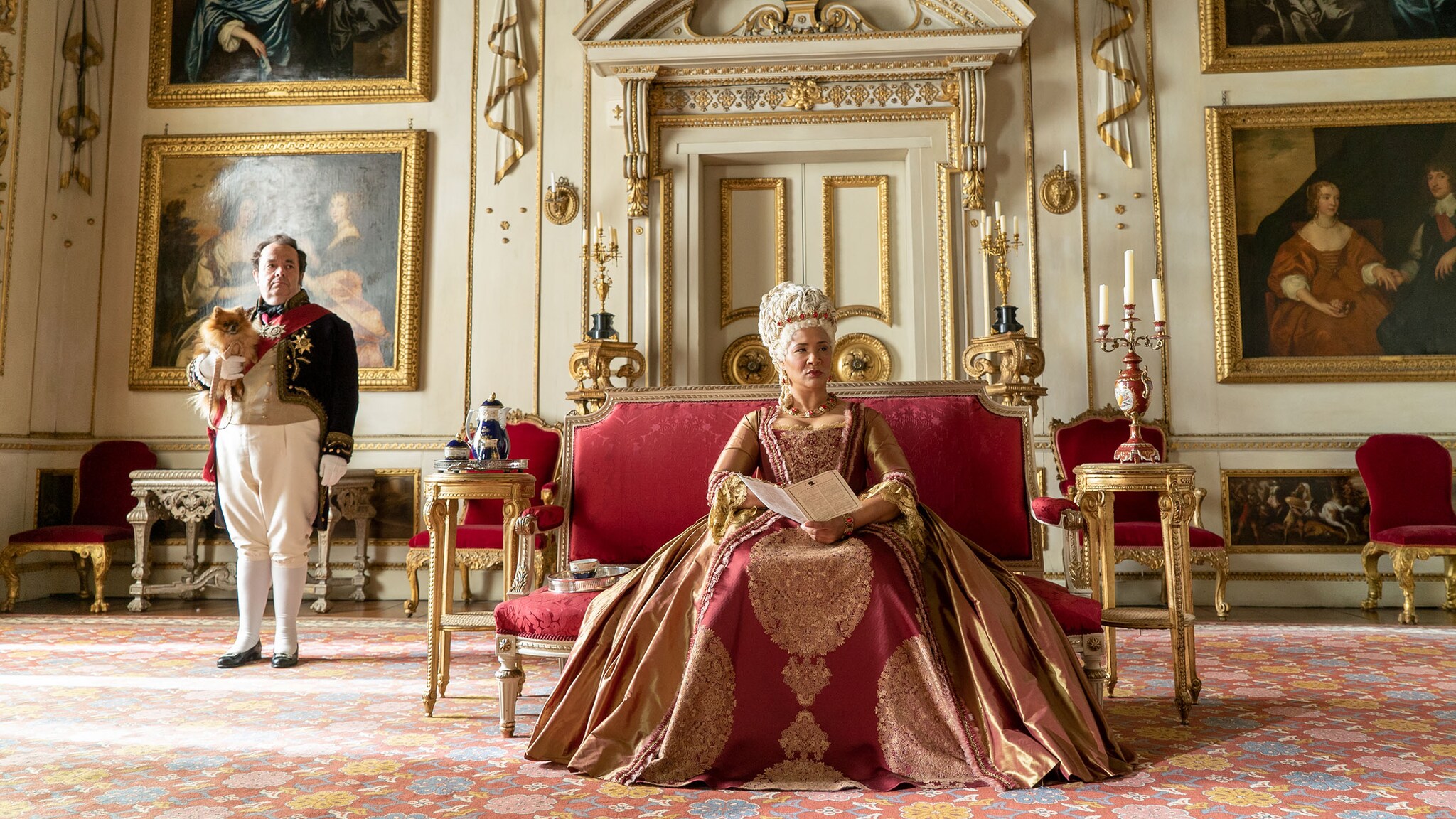 Eine Königin sitzt auf einem roten Samtsofa in einem Palast mit weiß-goldenem Dekor. Eine Königin sitzt auf einem roten Samtsofa in einem Palast mit weiß-goldenem Dekor.