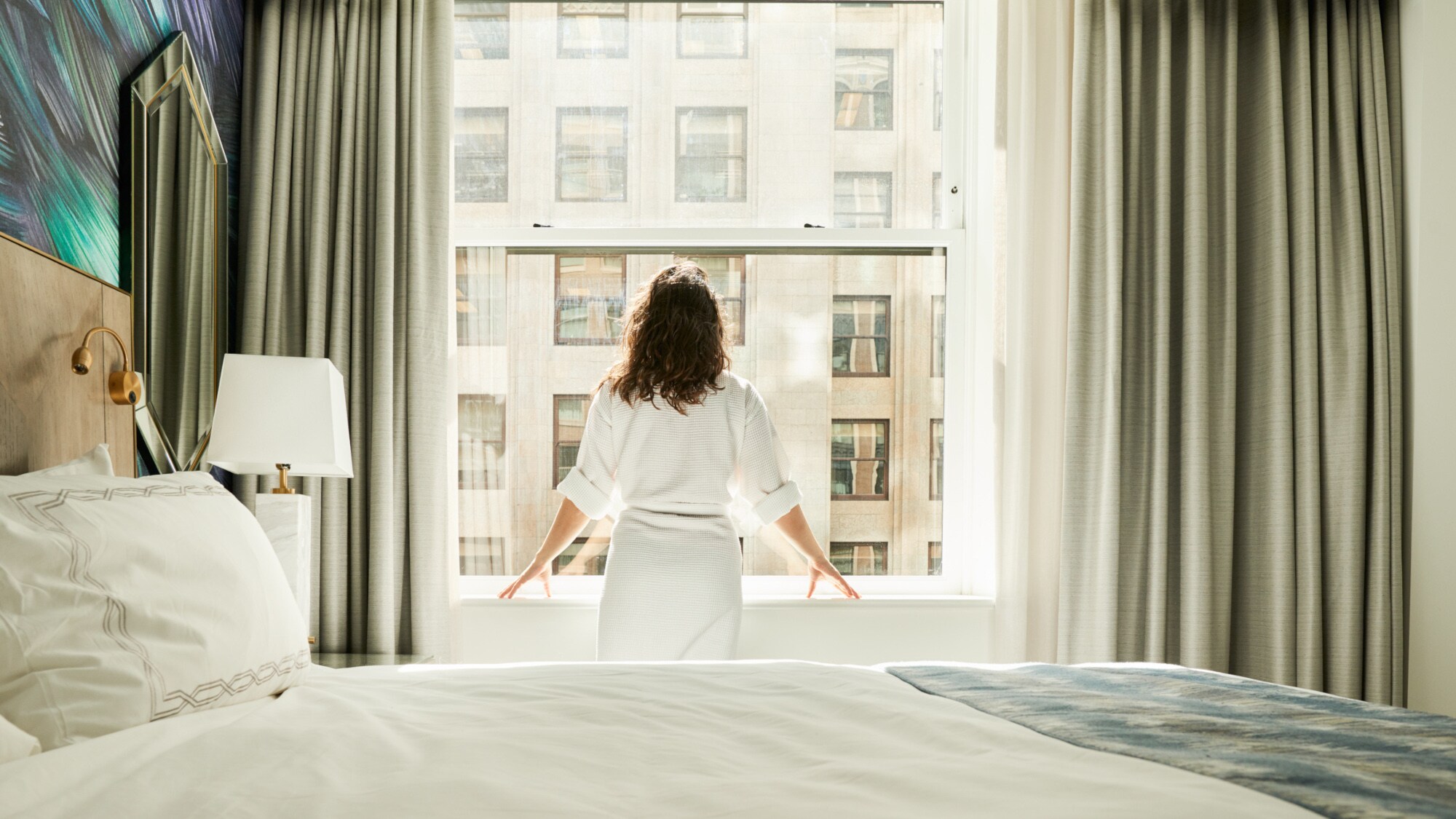 Rückansicht einer Frau im Bademantel, die am Fenster eines Hotelzimmers steht. Rückansicht einer Frau im Bademantel, die am Fenster eines Hotelzimmers steht.