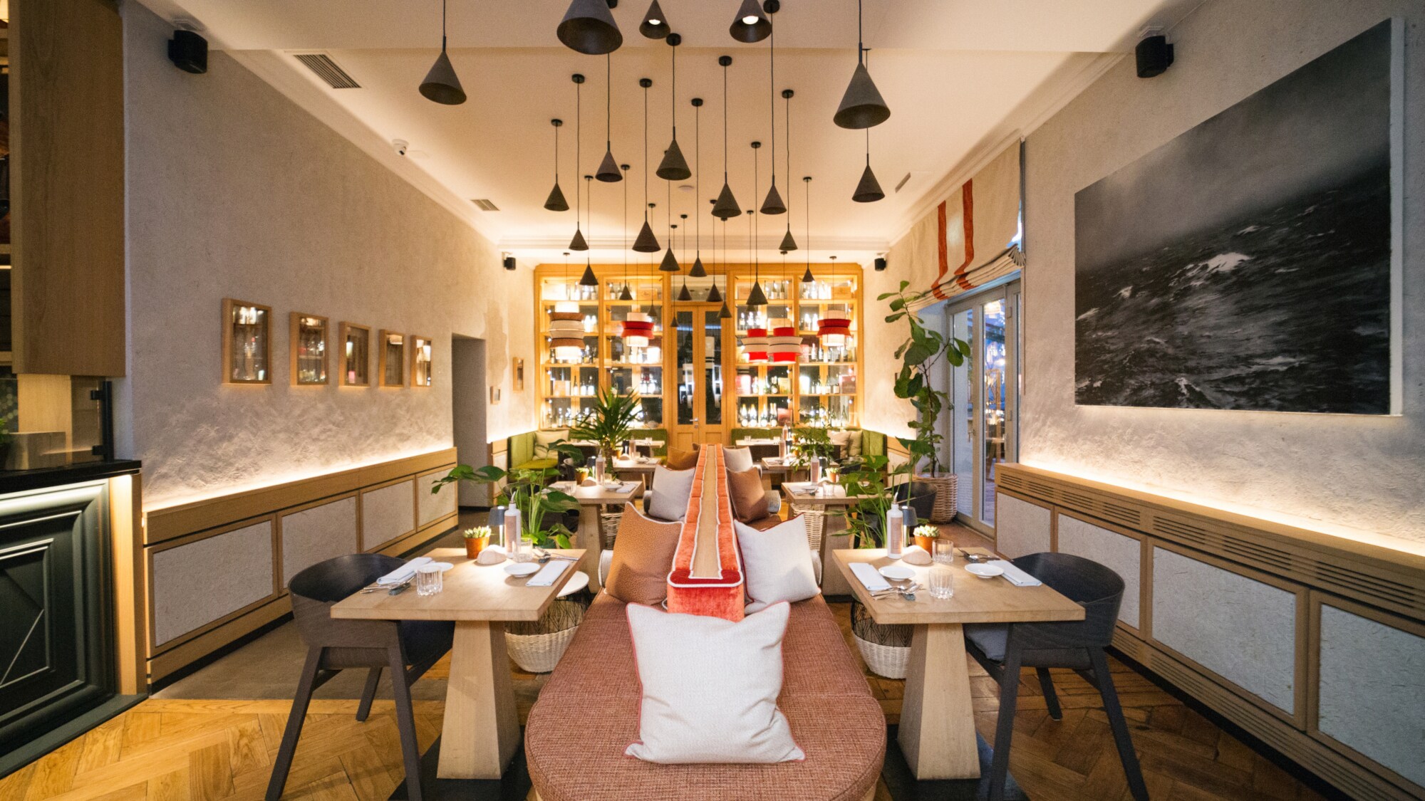 Hell ausgeleuchteter Innenraum des Restaurants Beetle von Feinkost Käfer in München mit Holztischen und einer Sitzbank im Mittelpunkt.